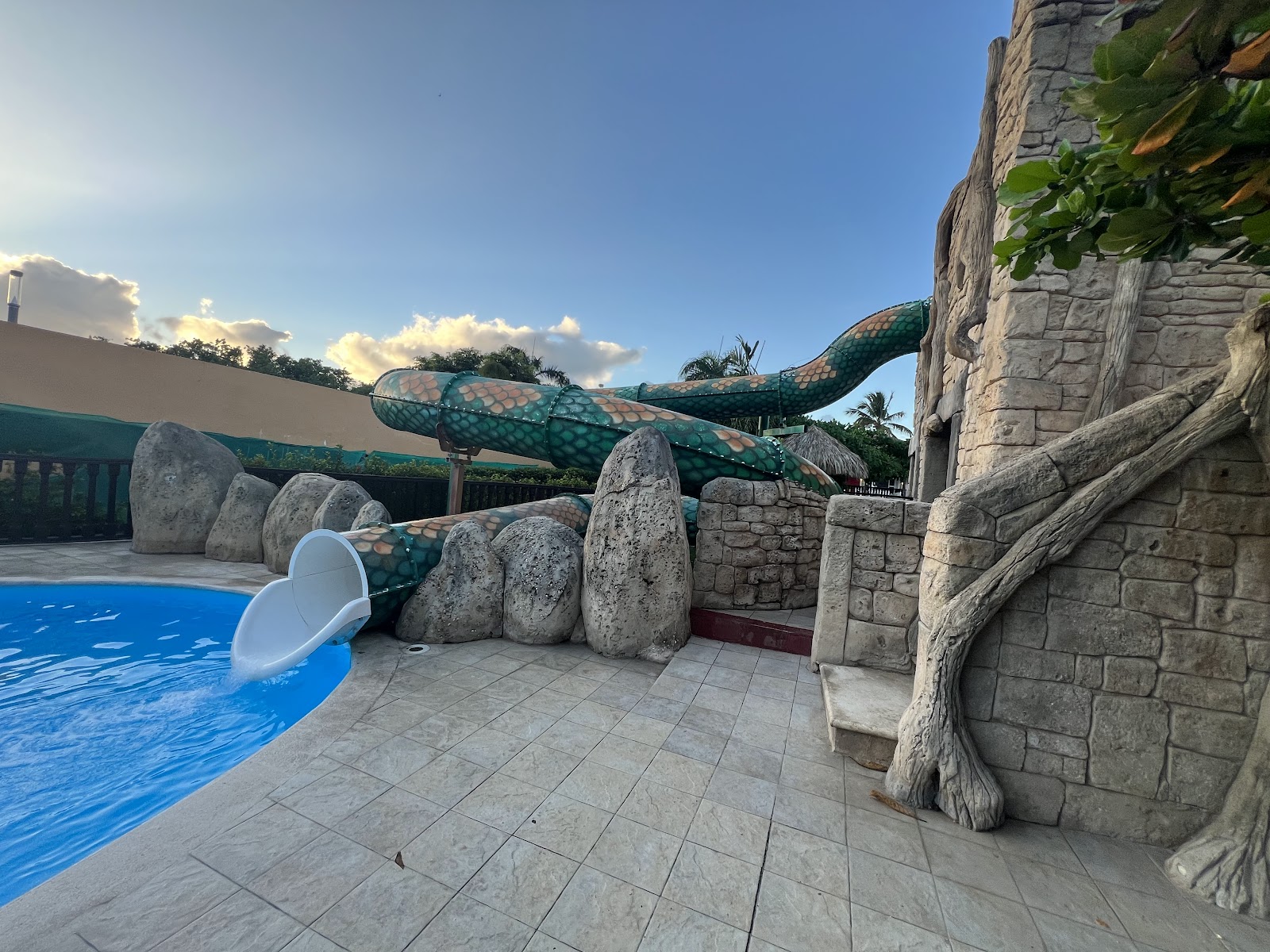 Themed water slide with giant serpent sculpture twists above pool area surrounded by stone structures and boulders.