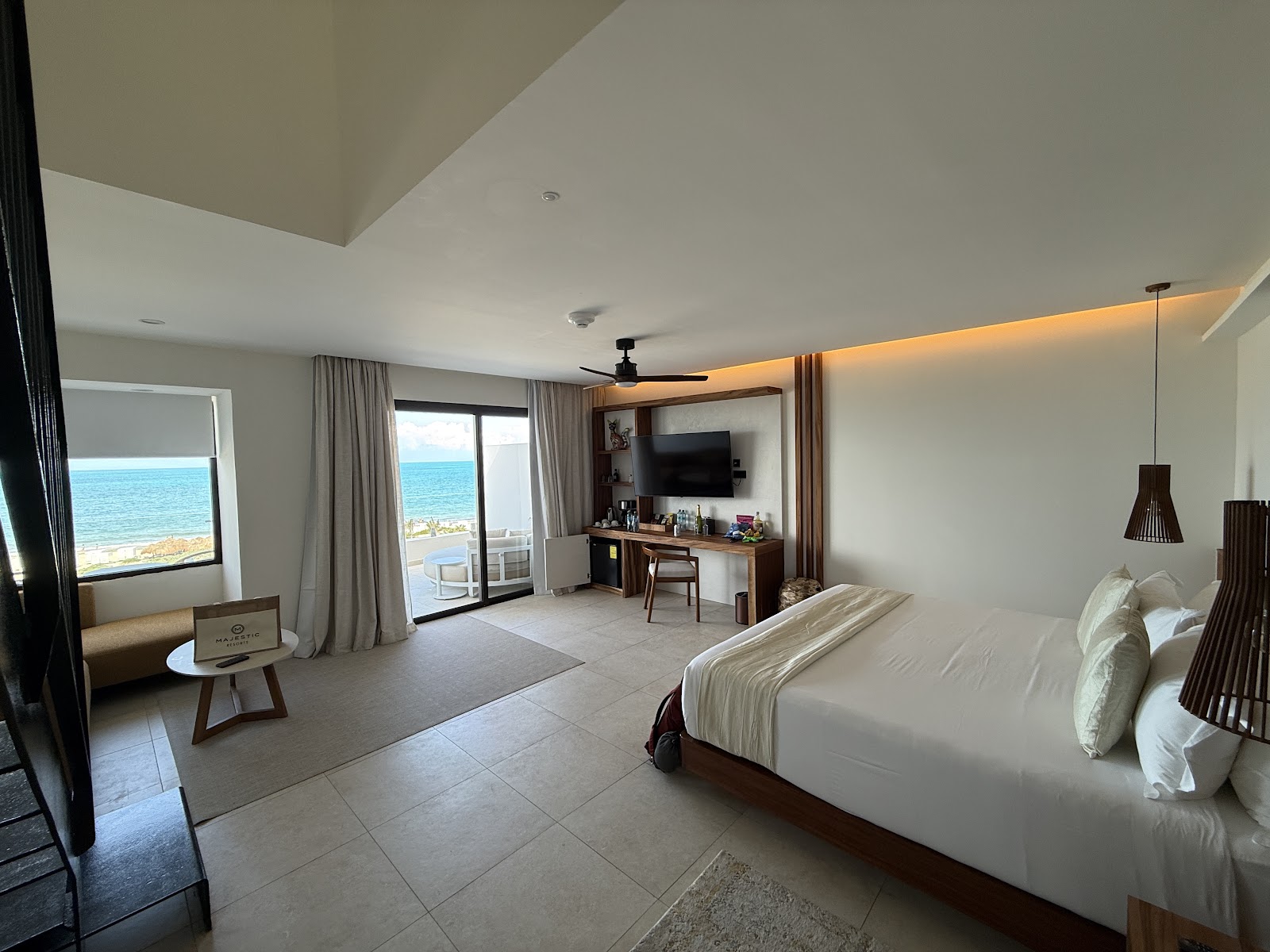 Oceanfront suite with king bed, work desk, flat-screen TV, and balcony overlooking turquoise water at Majestic Mirage Costa Mujeres.