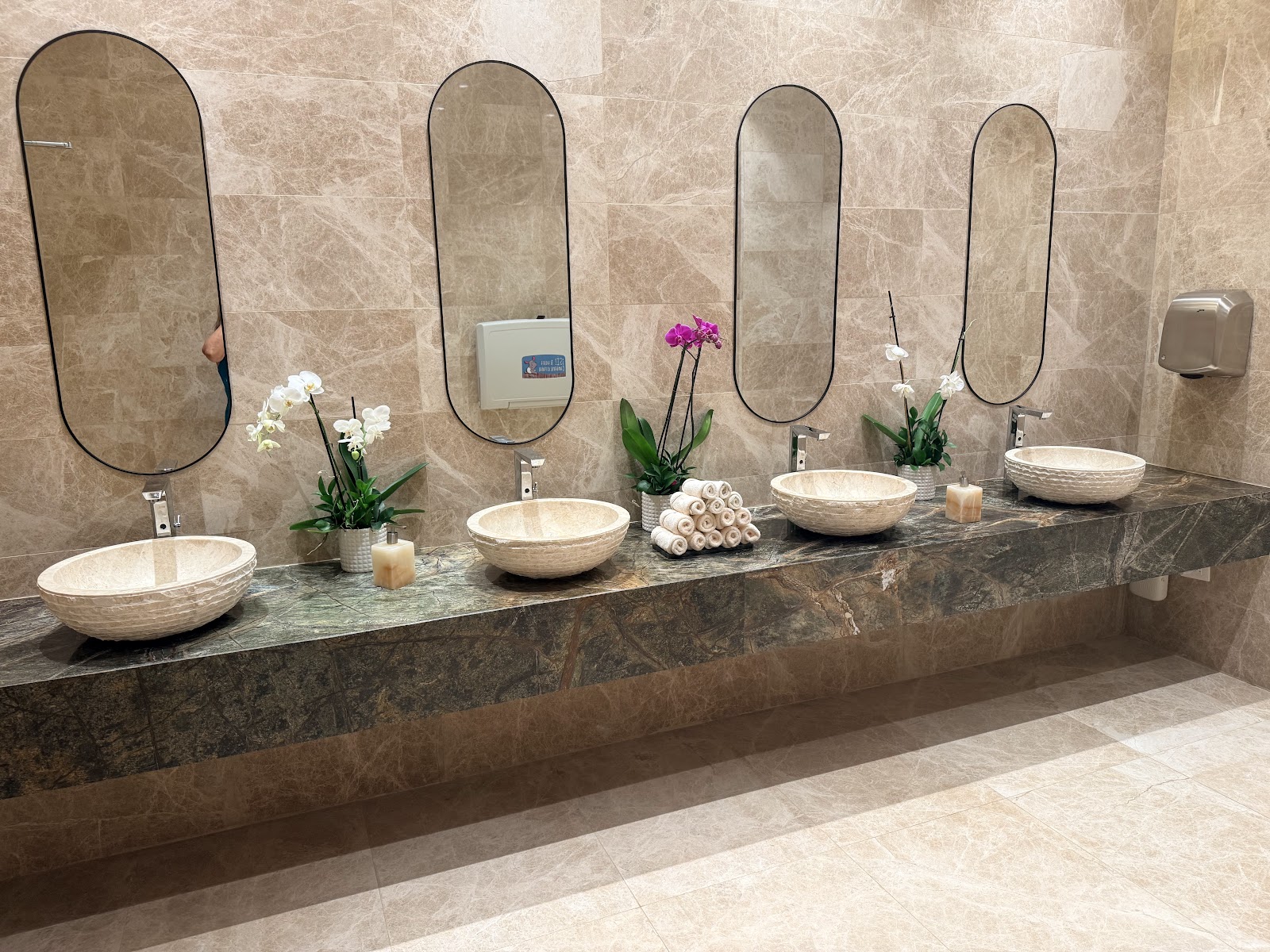 Luxury bathroom vanity with four round vessel sinks, arched mirrors, potted orchids, rolled towels, and marble countertop at Majestic Mirage Costa Mujeres.