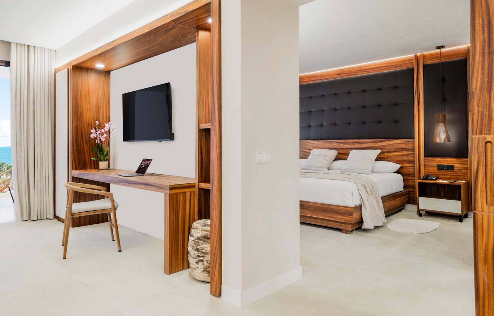 Modern resort suite with wooden four-poster bed, work desk with TV, and ocean view through open archway at Majestic Mirage Costa Mujeres.