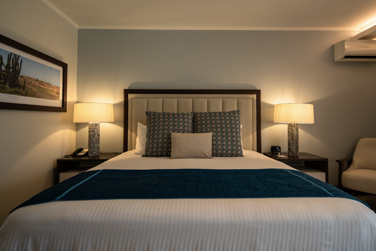 Resort bedroom with king bed, upholstered headboard, matching nightstands with lamps, and a desert landscape photograph on the wall.
