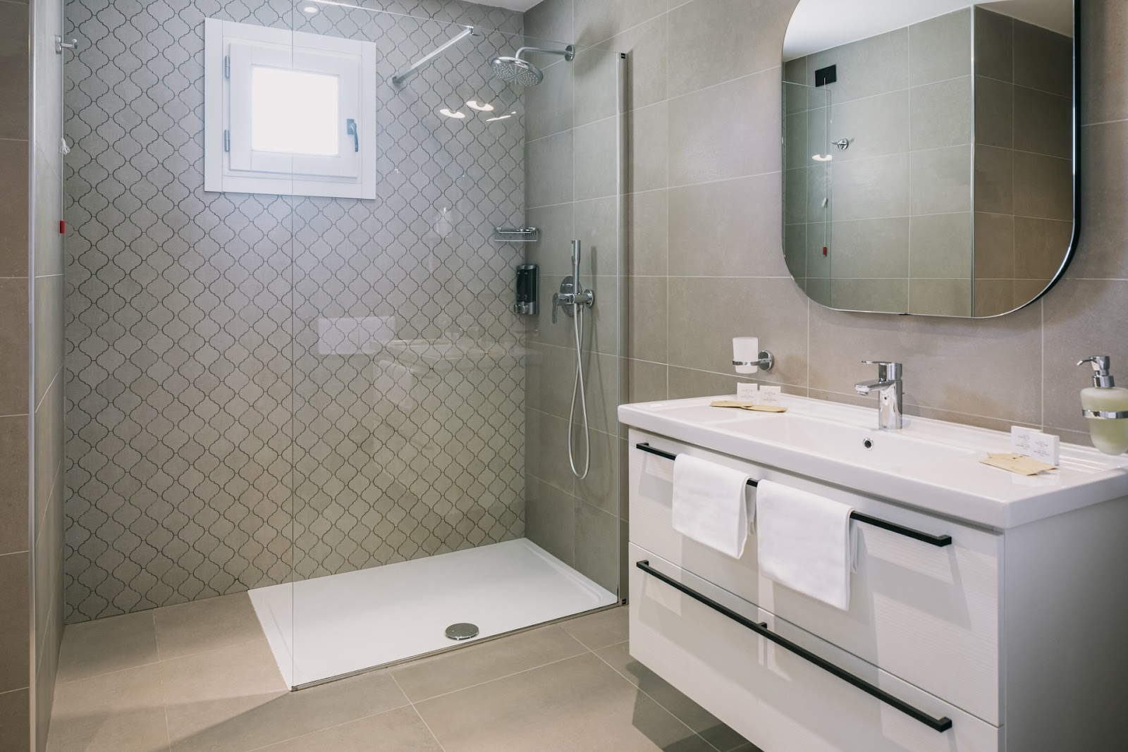 Modern bathroom with walk-in shower, white vanity with dual sinks, curved mirror, and geometric tile accents.