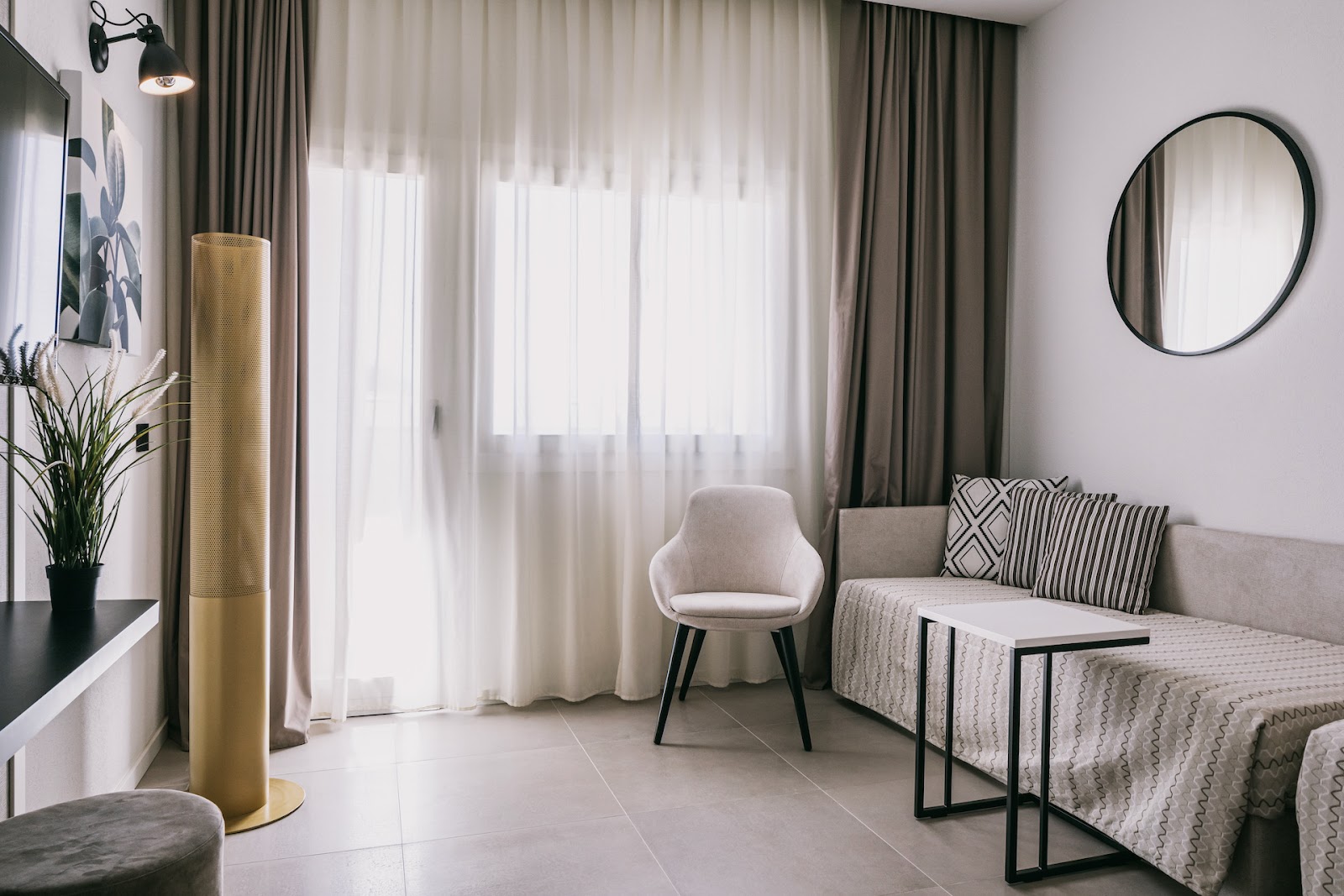 Modern lobby lounge with gray upholstered wingback chairs arranged around small tables, potted plants, and large windows at Mangia's Himera Resort.