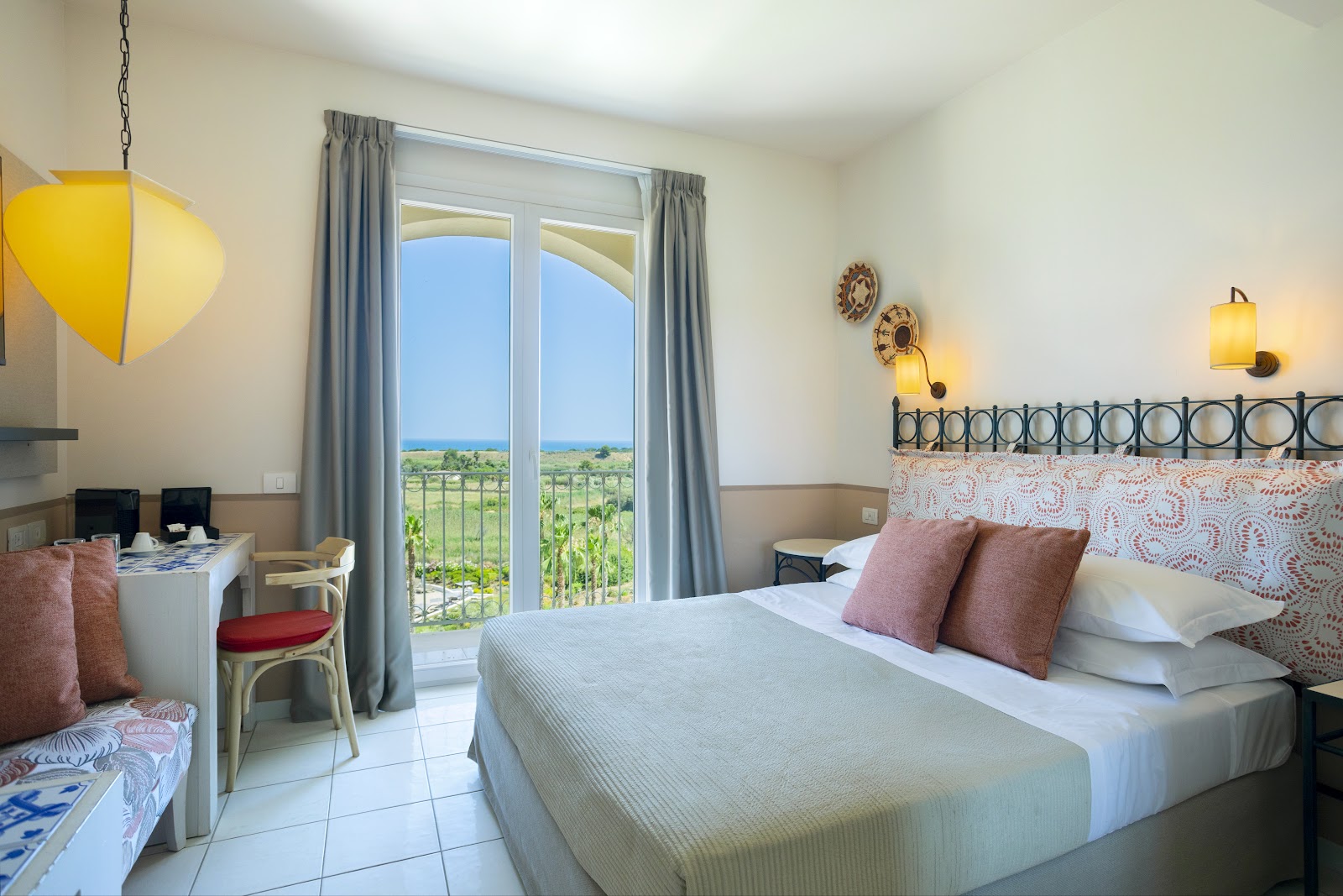 Bright bedroom with double bed, work desk, and glass doors opening to balcony overlooking vineyard countryside.