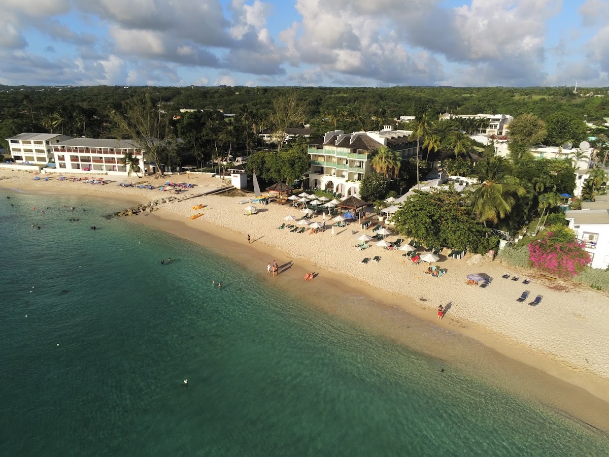 Mango Bay Hotel beachfront with turquoise water, sandy beach lined with loungers, and palm trees backing lush green hillside.