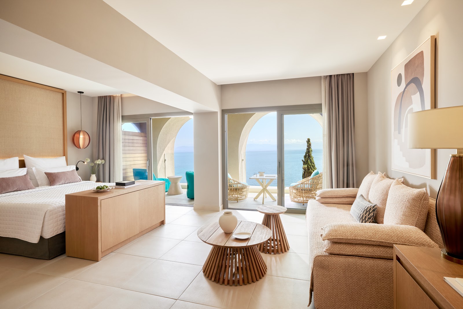 Modern suite at MarBella with bed, seating area, and ocean view through floor-to-ceiling doors opening to a balcony.