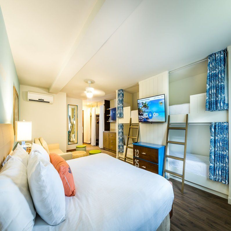 Family room with queen bed, bunk beds with blue curtains, wall-mounted TV, and air conditioning at Margaritaville Beach Resort Playa Flamingo.