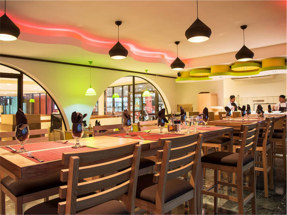 Modern dining room at Margaritaville Beach Resort with wooden tables, black pendant lights, and neon ceiling accent in warm tones.