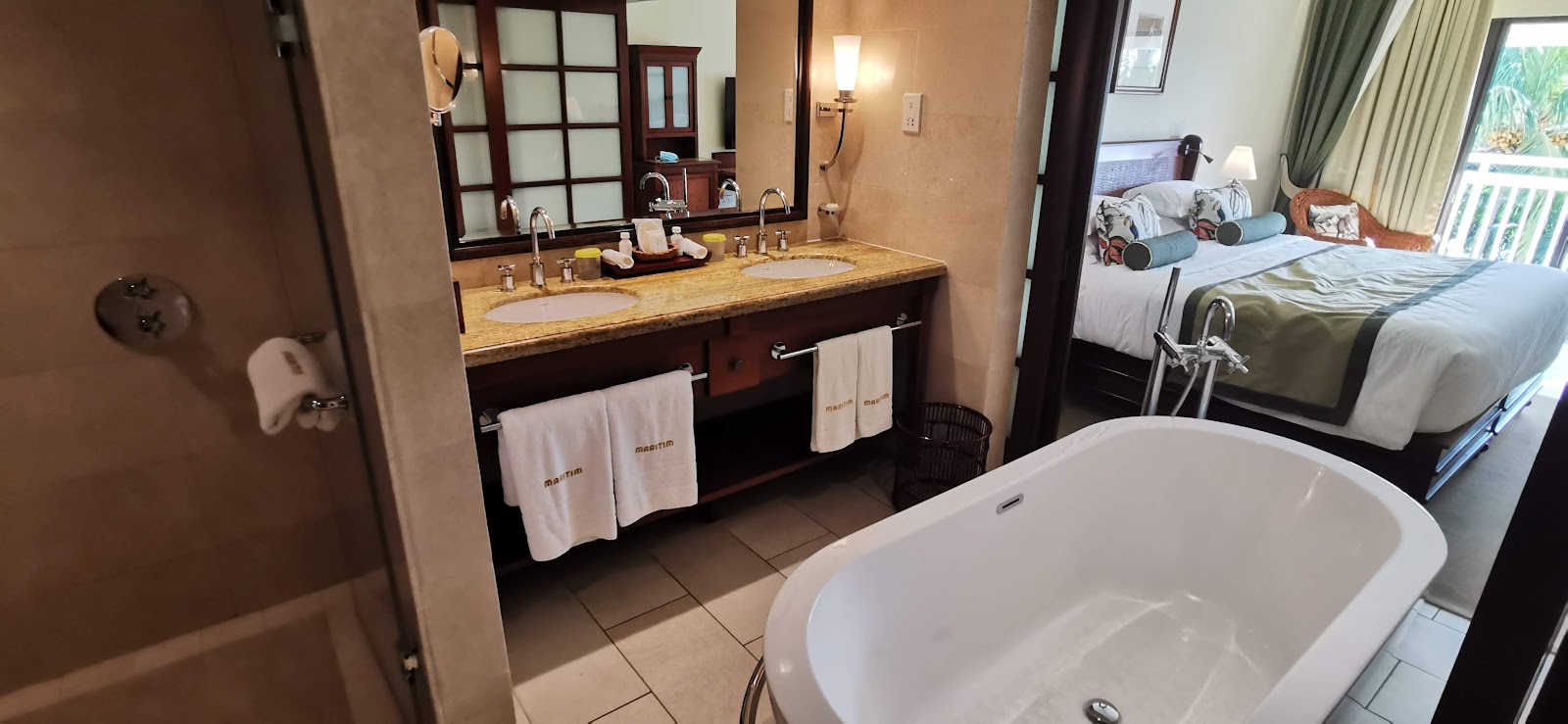 Bathroom with freestanding white tub, dark wood vanity with double sinks, large mirror, and glass shower enclosure with gridded doors.