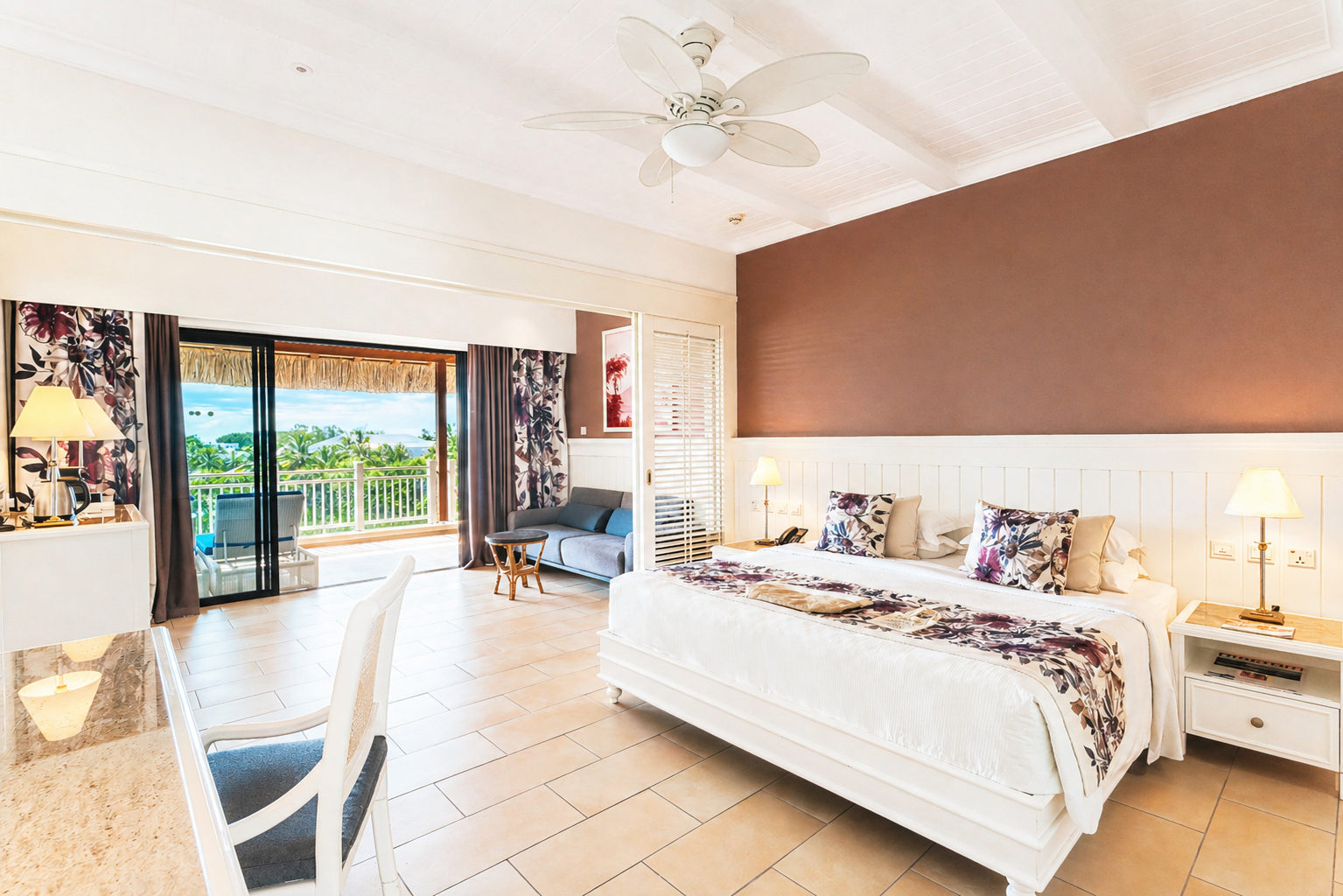 Spacious resort suite with beige sofa, wicker chairs, and glass doors opening to a beachfront terrace with ocean views.