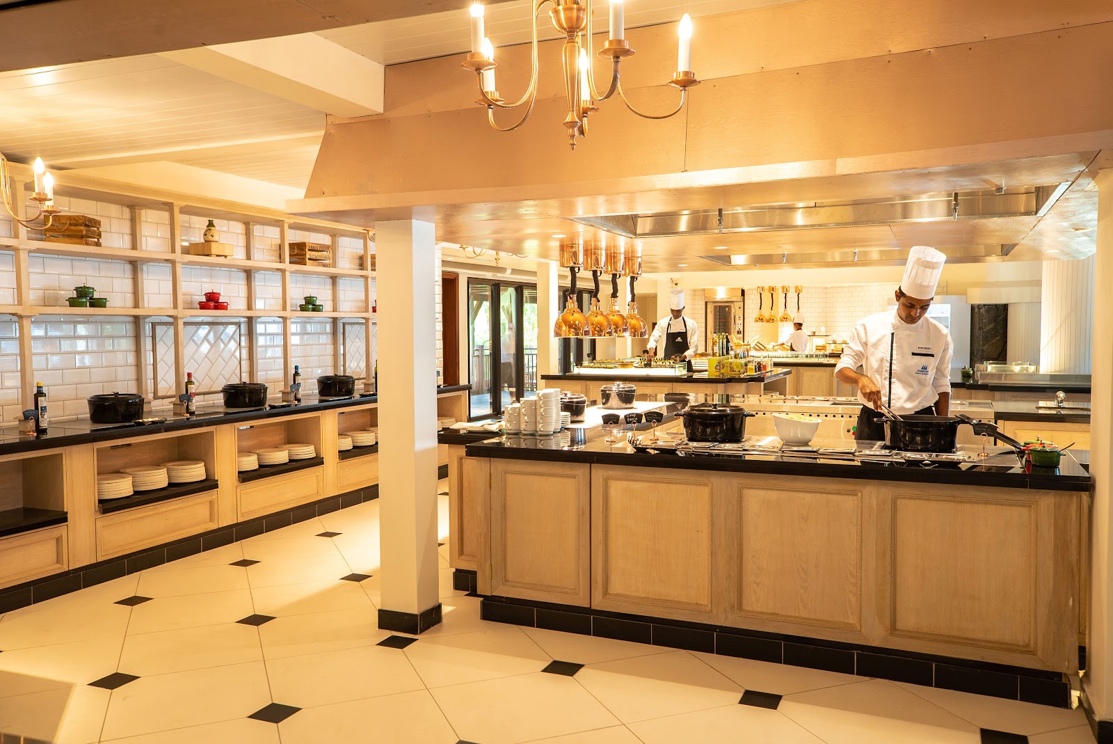 Chef works at a central counter in the open kitchen at Maritim Resort & Spa Mauritius, with cream-colored cabinetry and warm lighting throughout.