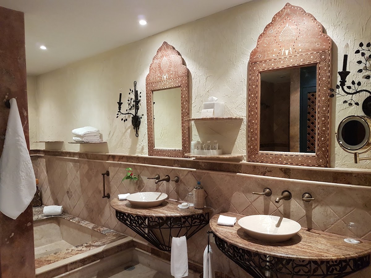 Spa-style bathroom with two vessel sinks, ornate copper-framed mirrors, textured stone walls, and decorative black metalwork accents.