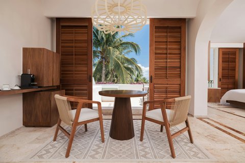 Modern suite interior with round wooden table, two chairs, and palm tree view through open louvered doors at Marriott All-Inclusive Riviera Maya.