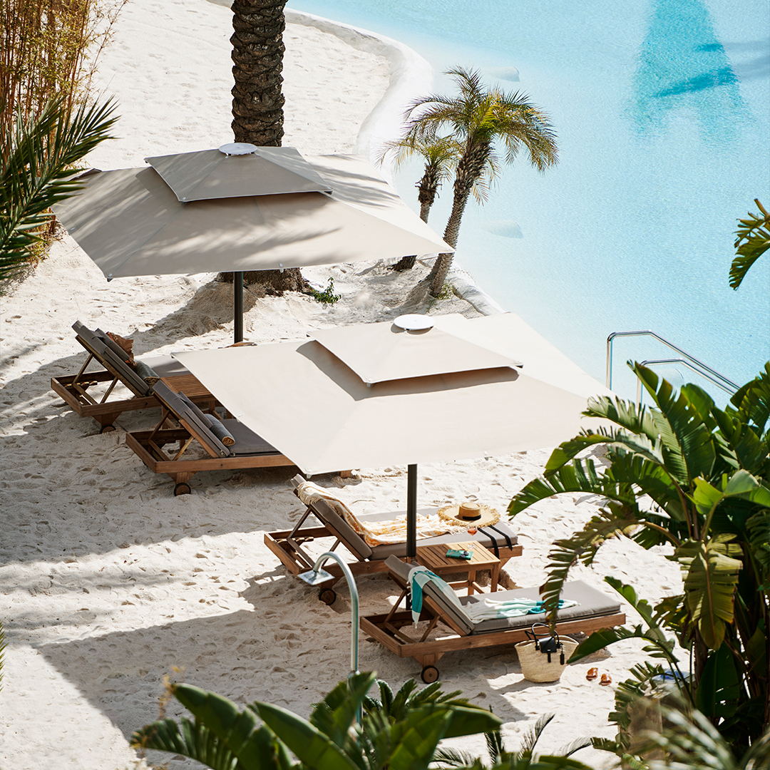 Wooden lounge chairs with umbrellas on white sand beach beside turquoise water at Maxx Royal Belek Golf Resort.