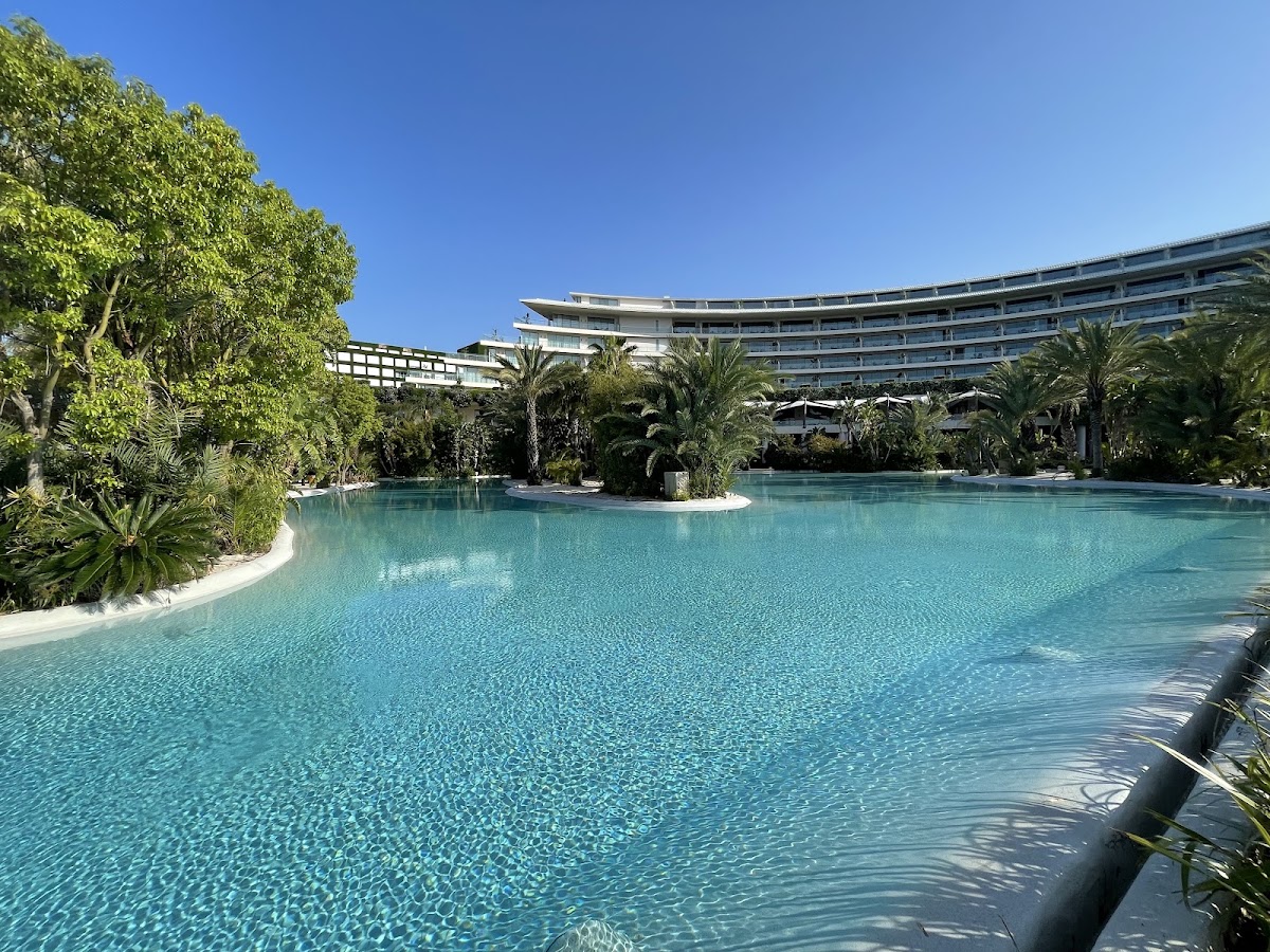 Large lagoon-style pool with turquoise water surrounded by palm trees and tropical landscaping at Maxx Royal Belek Golf Resort.