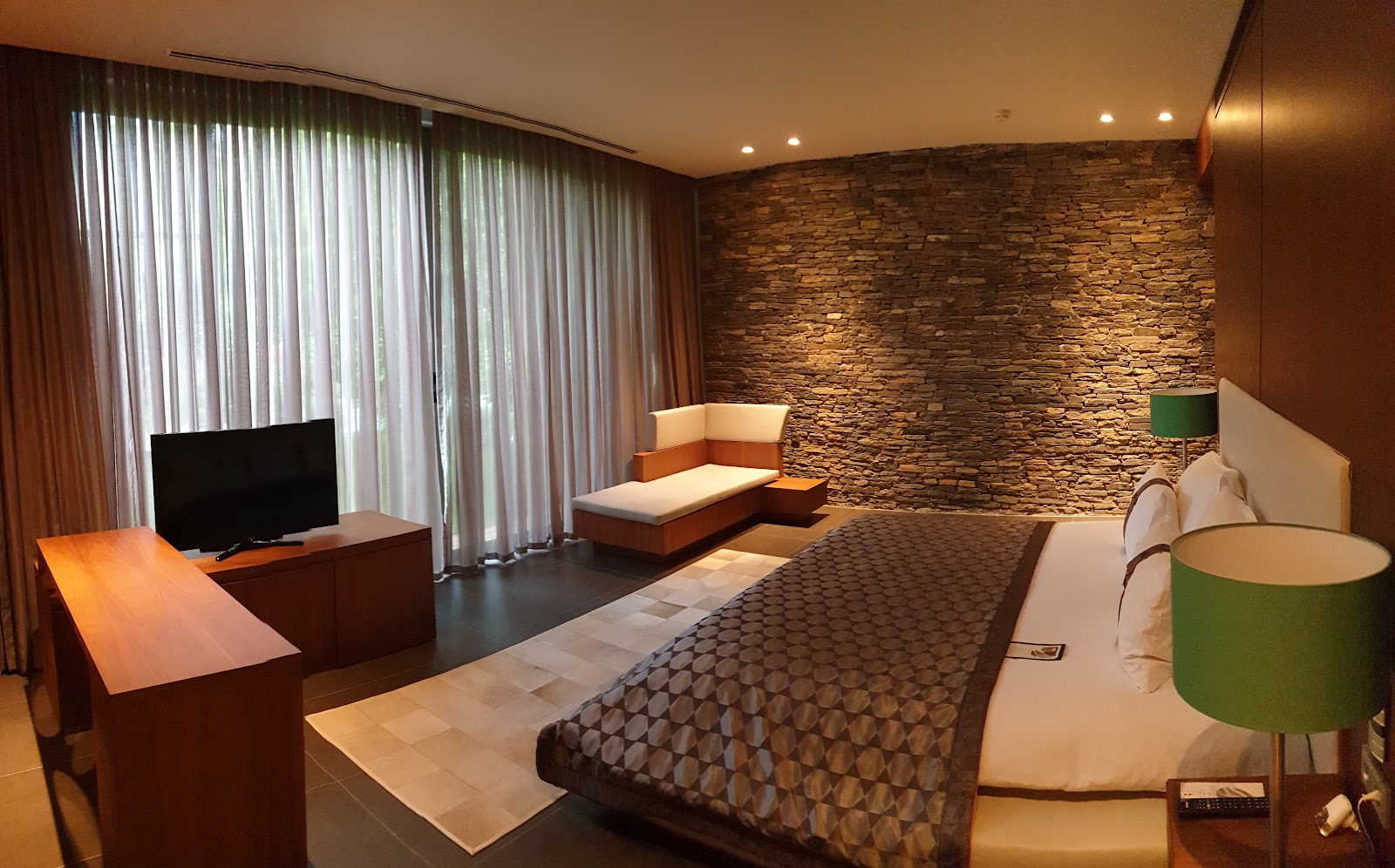 Resort bedroom with geometric patterned wallpaper, queen bed, orange accent chair, and sliding glass doors opening to a balcony overlooking coastline.