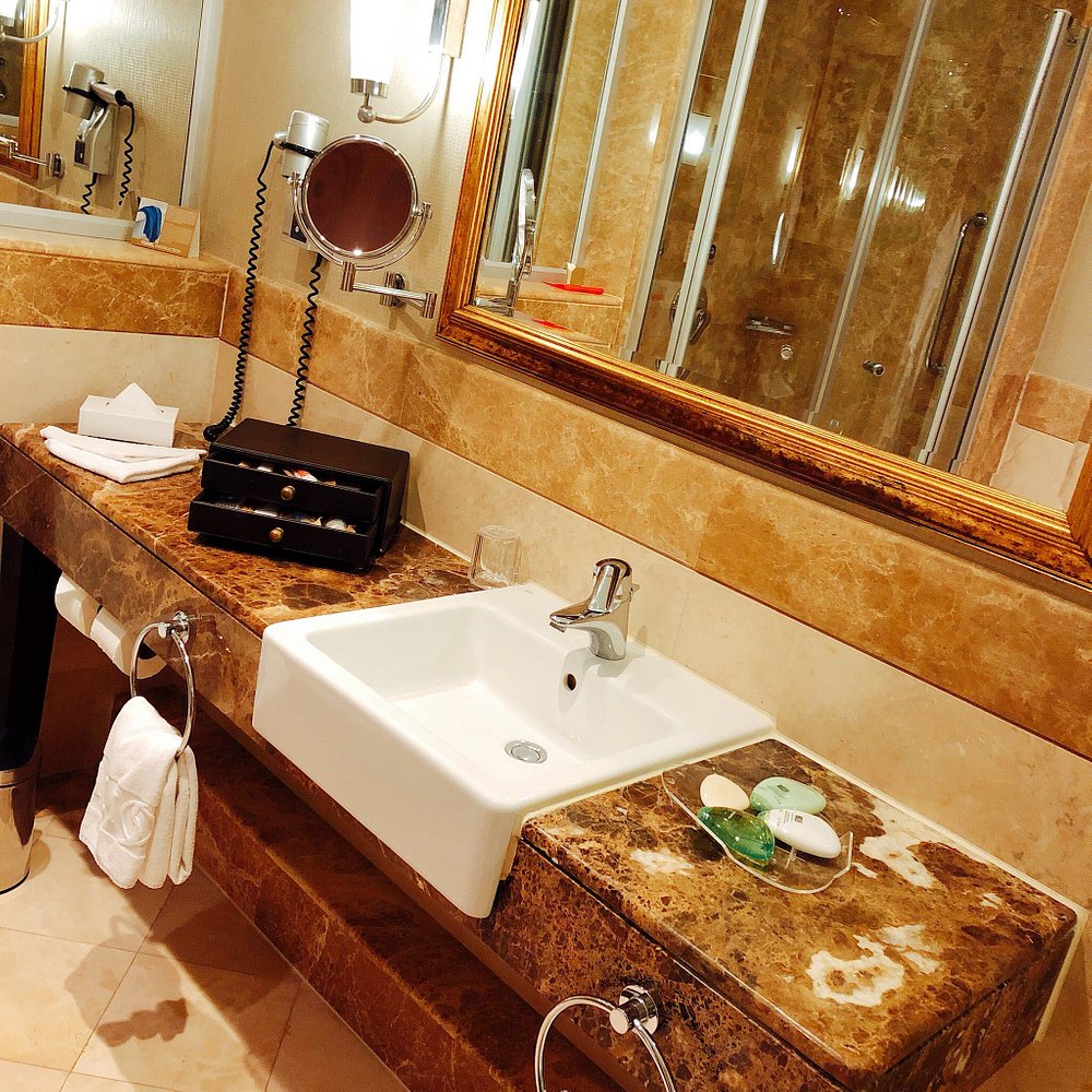 Bathroom with brown marble countertop, white rectangular sink, large mirror with gold frame, and glass shower enclosure.