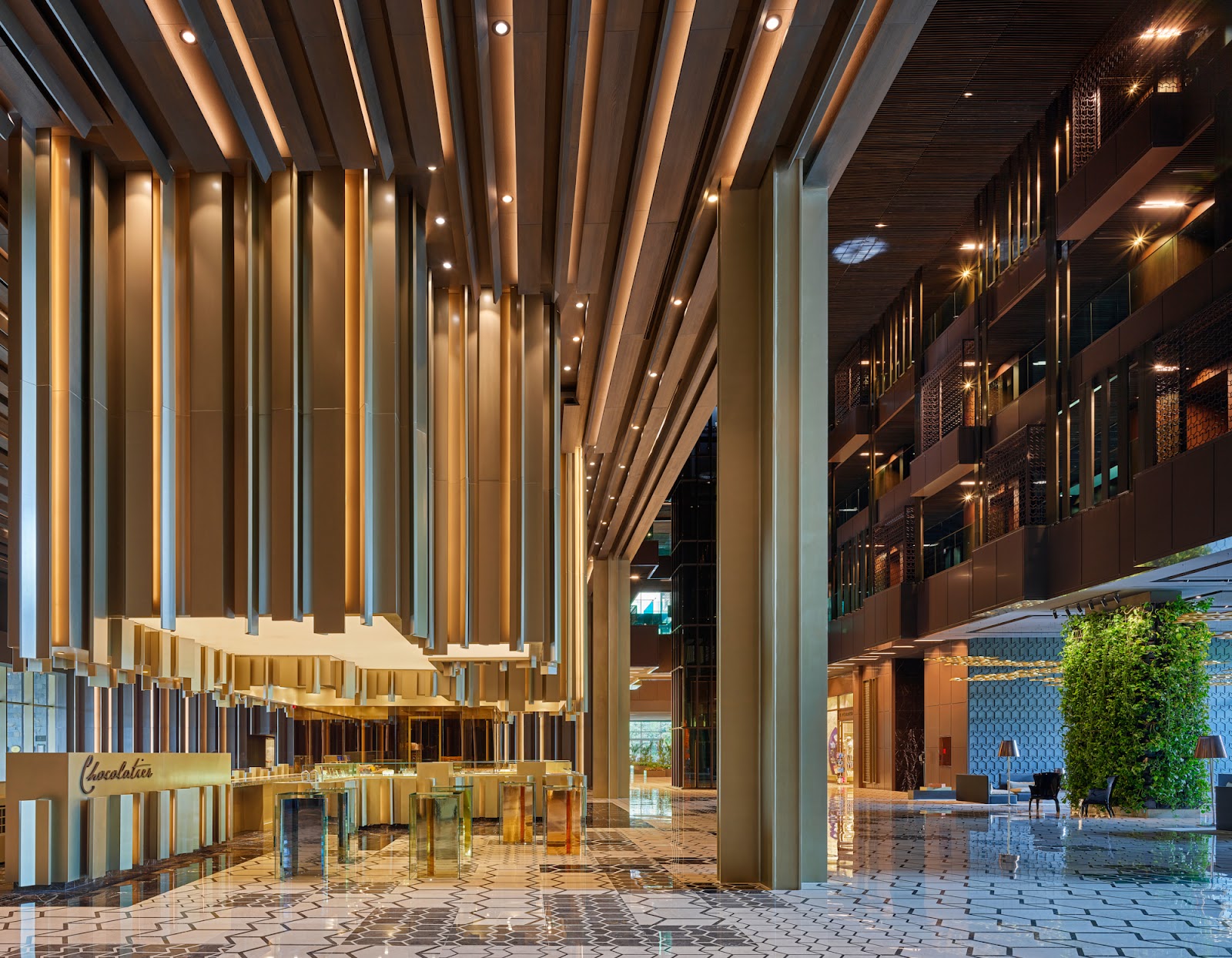 Modern dining hall with layered white ceiling, green-tiled bar, potted plants, and geometric floor at Maxx Royal Kemer Resort.
