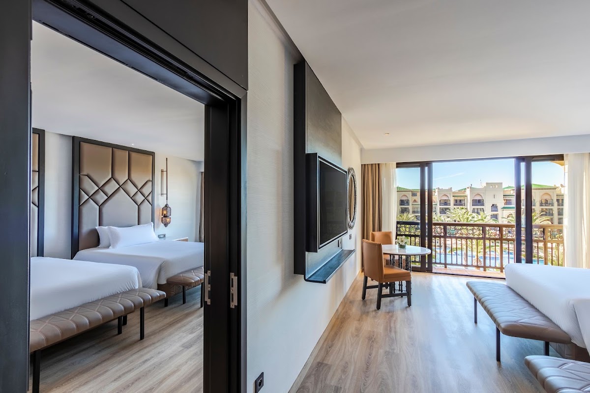 Spacious suite at Mazagan Beach & Golf Resort with two beds, flat-screen TV, and balcony overlooking resort grounds and ocean.
