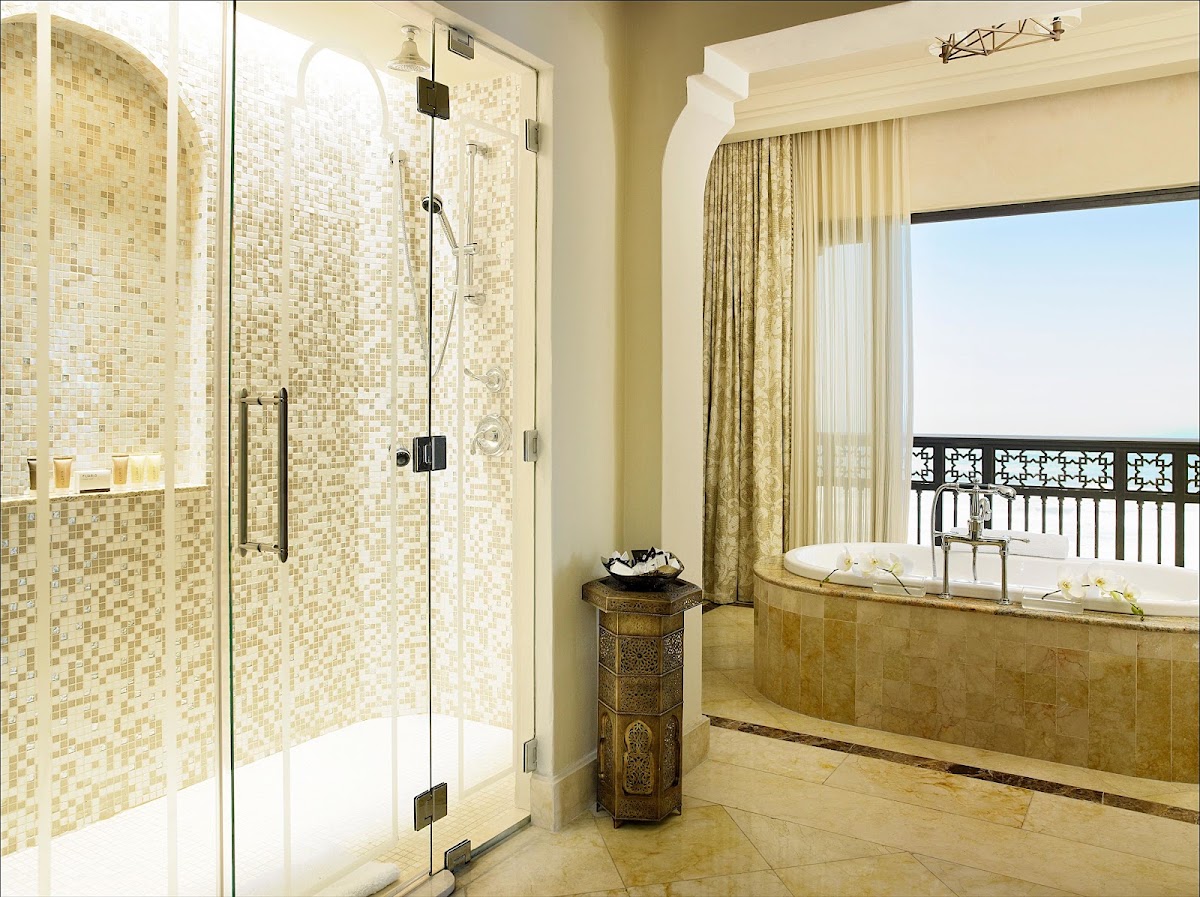 Luxury bathroom with glass-enclosed shower, soaking tub, and balcony overlooking ocean at Mazagan Beach & Golf Resort.