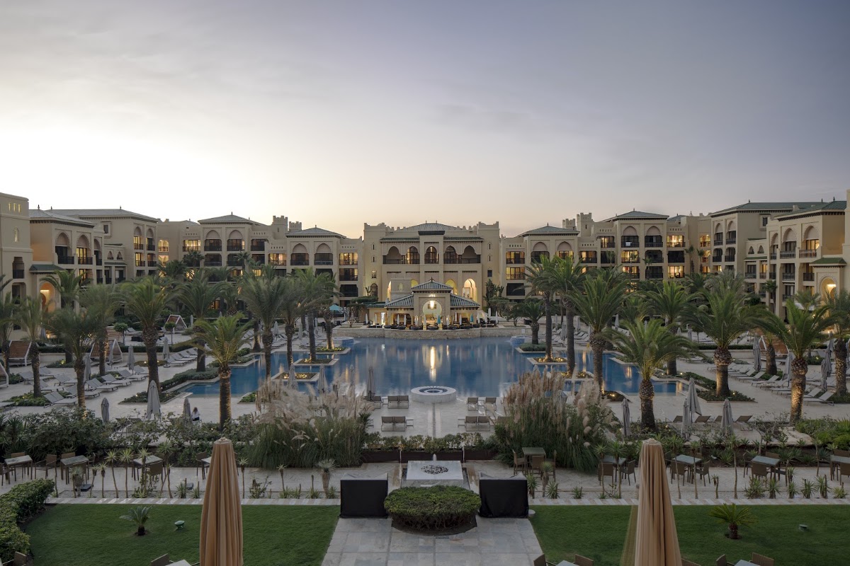 Central courtyard with illuminated blue pool surrounded by palm trees and Moorish-style resort buildings at dusk.