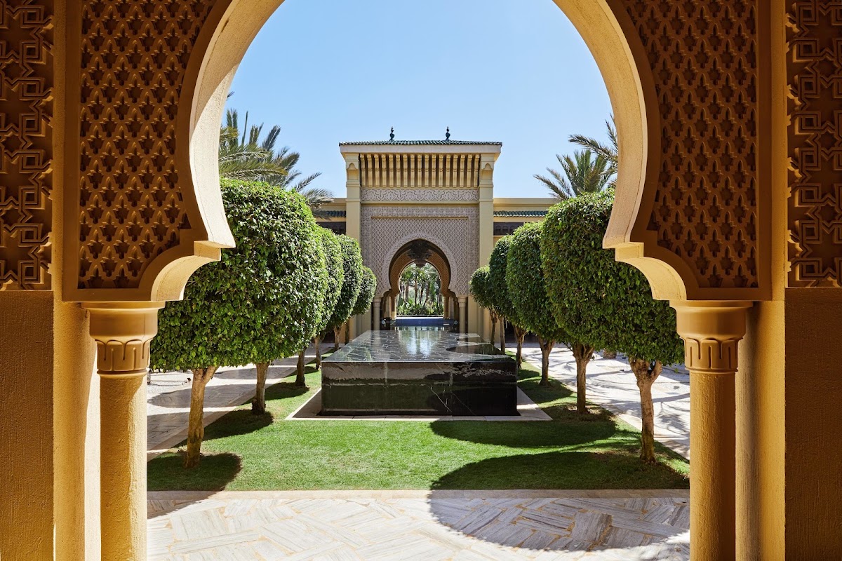 Arched doorway framing a Moroccan courtyard with manicured gardens, a central fountain, and ornate palace architecture beyond at Mazagan Beach & Golf Resort.