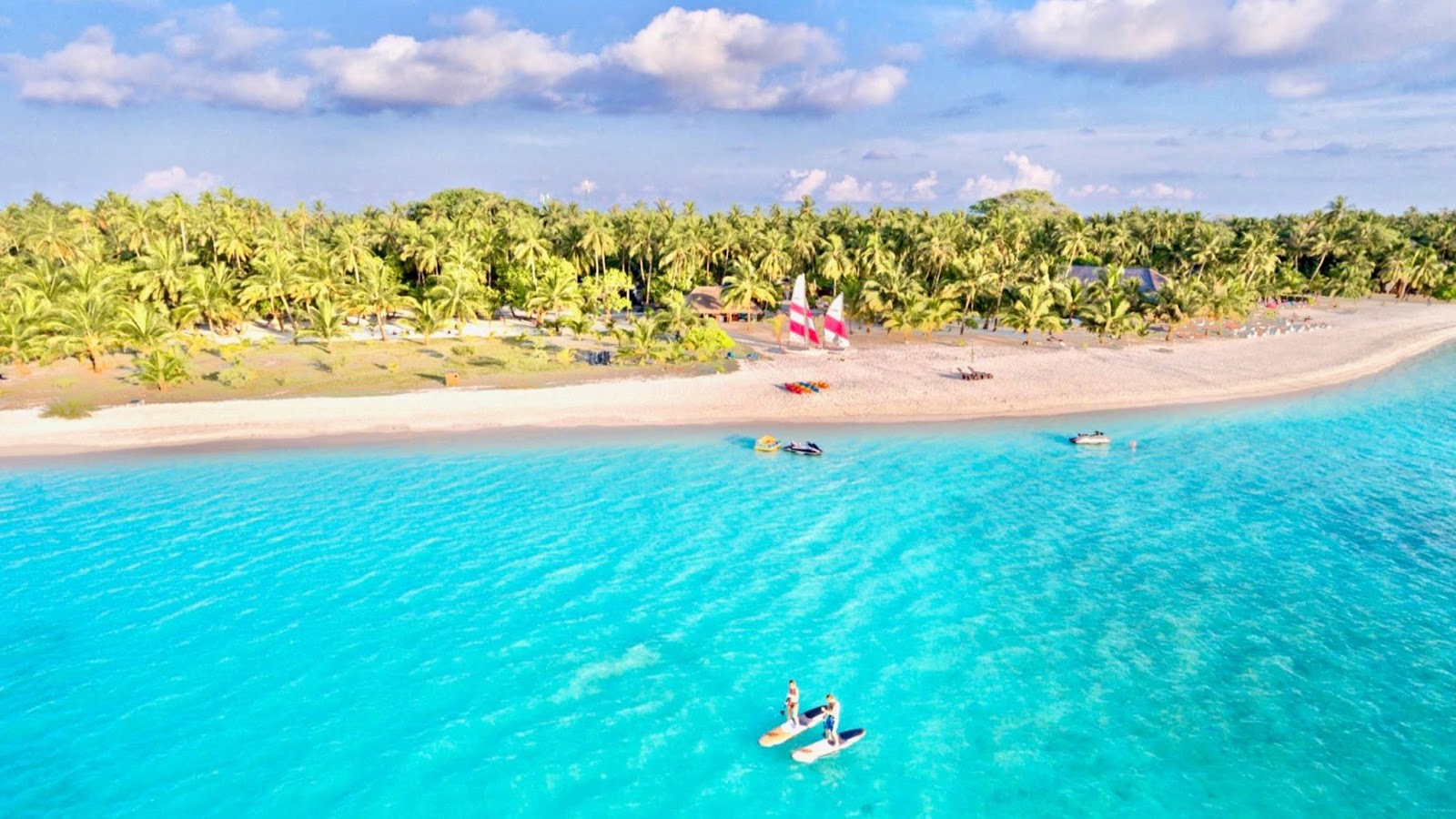 Illuminated bungalows with thatched roofs and wooden structures sit on sand surrounded by palm trees at dusk at Meeru Maldives Resort.