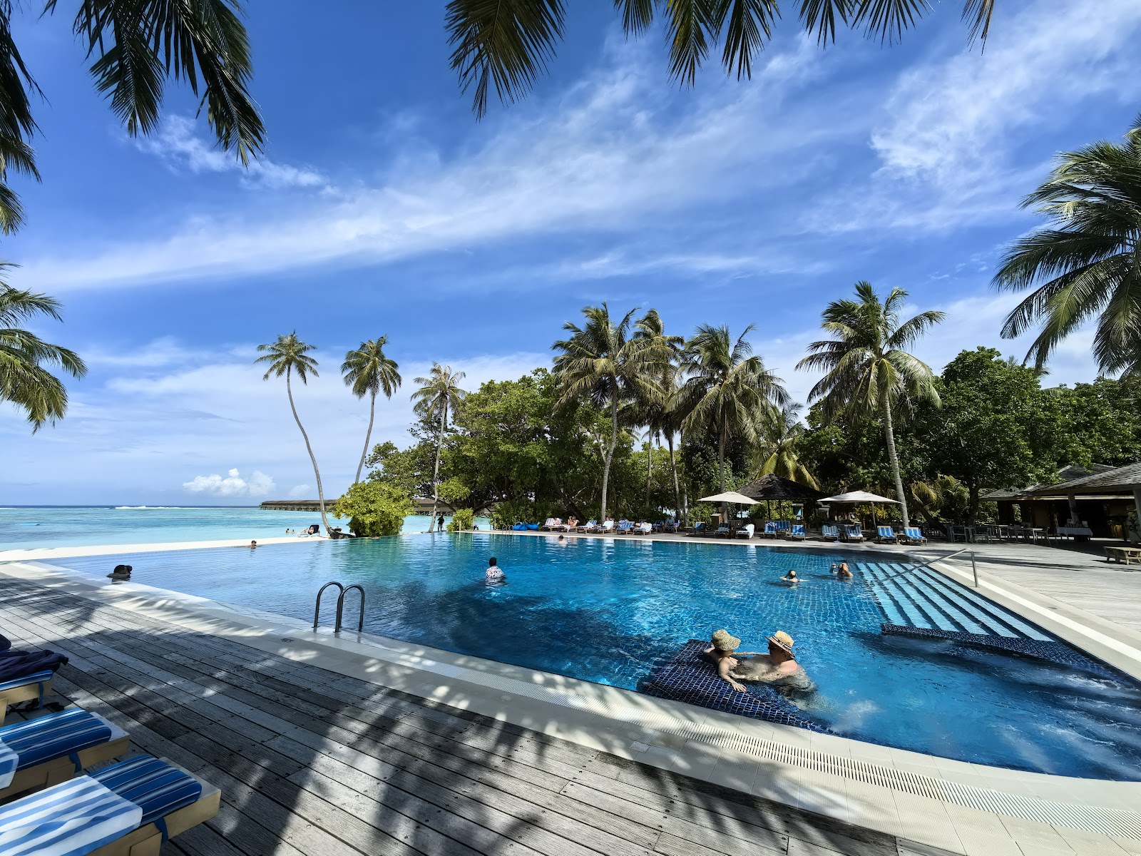 Palm trees and lush tropical vegetation frame a view of turquoise lagoon and distant islands under clear blue sky at Meeru Maldives Resort.