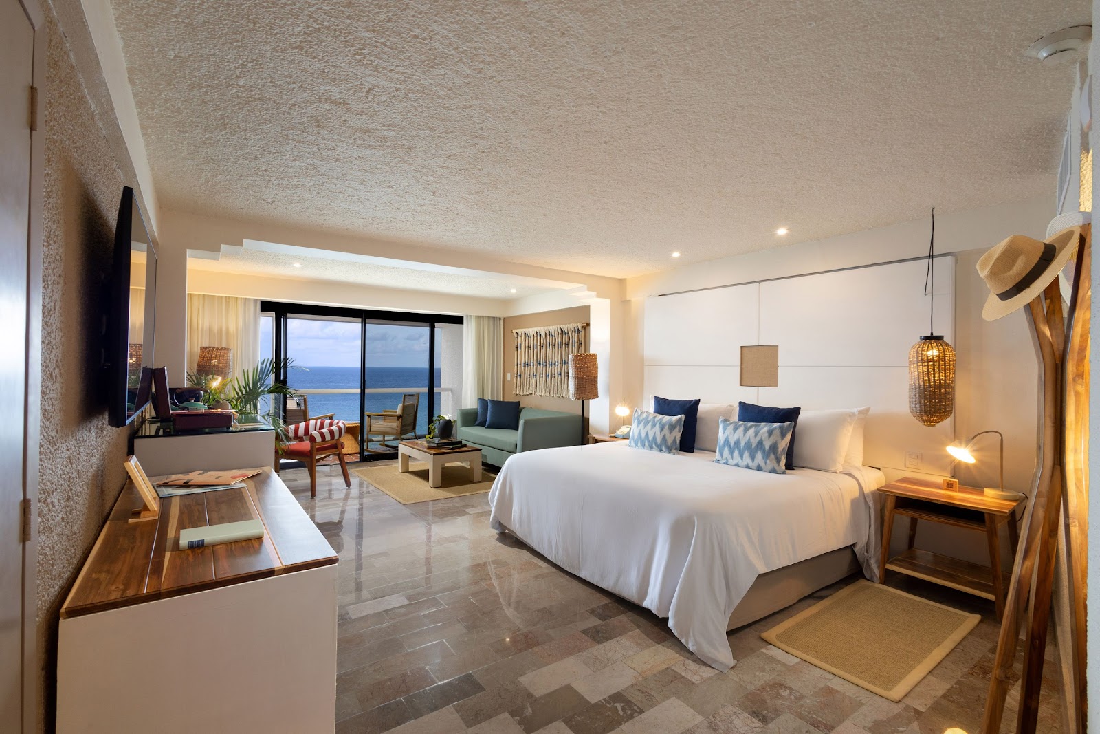 Spacious resort bedroom with canopy bed, turquoise accents, and seating area overlooking tropical grounds.