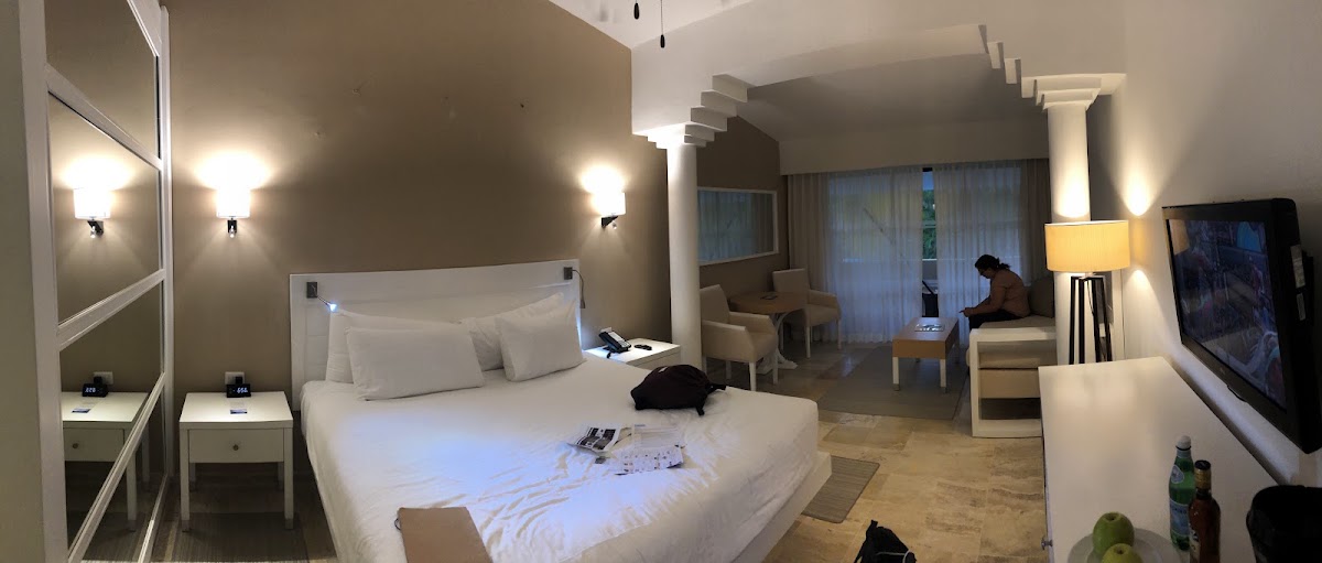Spacious resort suite with white bedding, sitting area, and glass doors opening to a balcony overlooking the grounds.