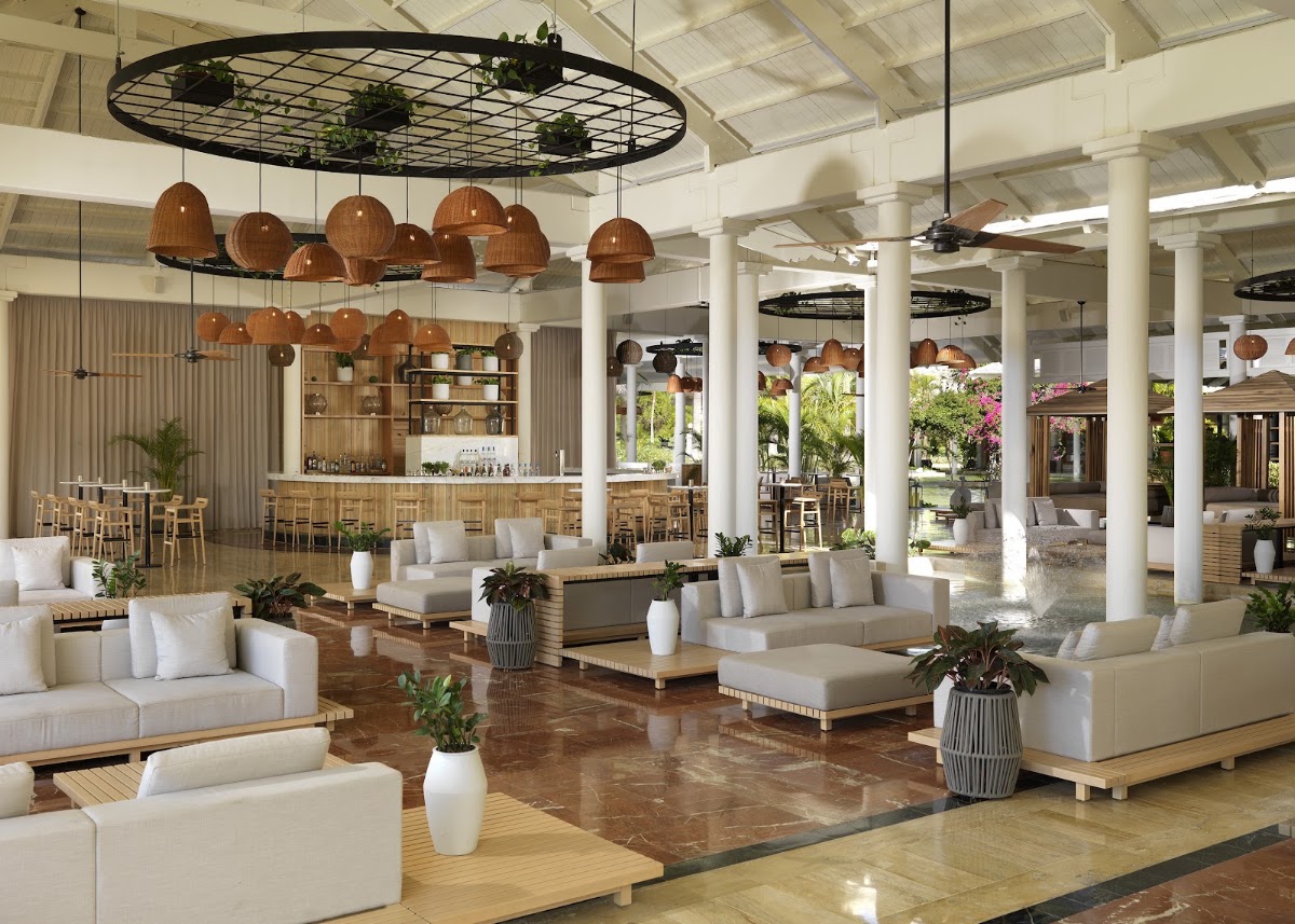 Open-air lobby with cream seating areas, wooden pendant lights, white columns, and garden views at Meliá Punta Cana Beach Wellness Inclusive.