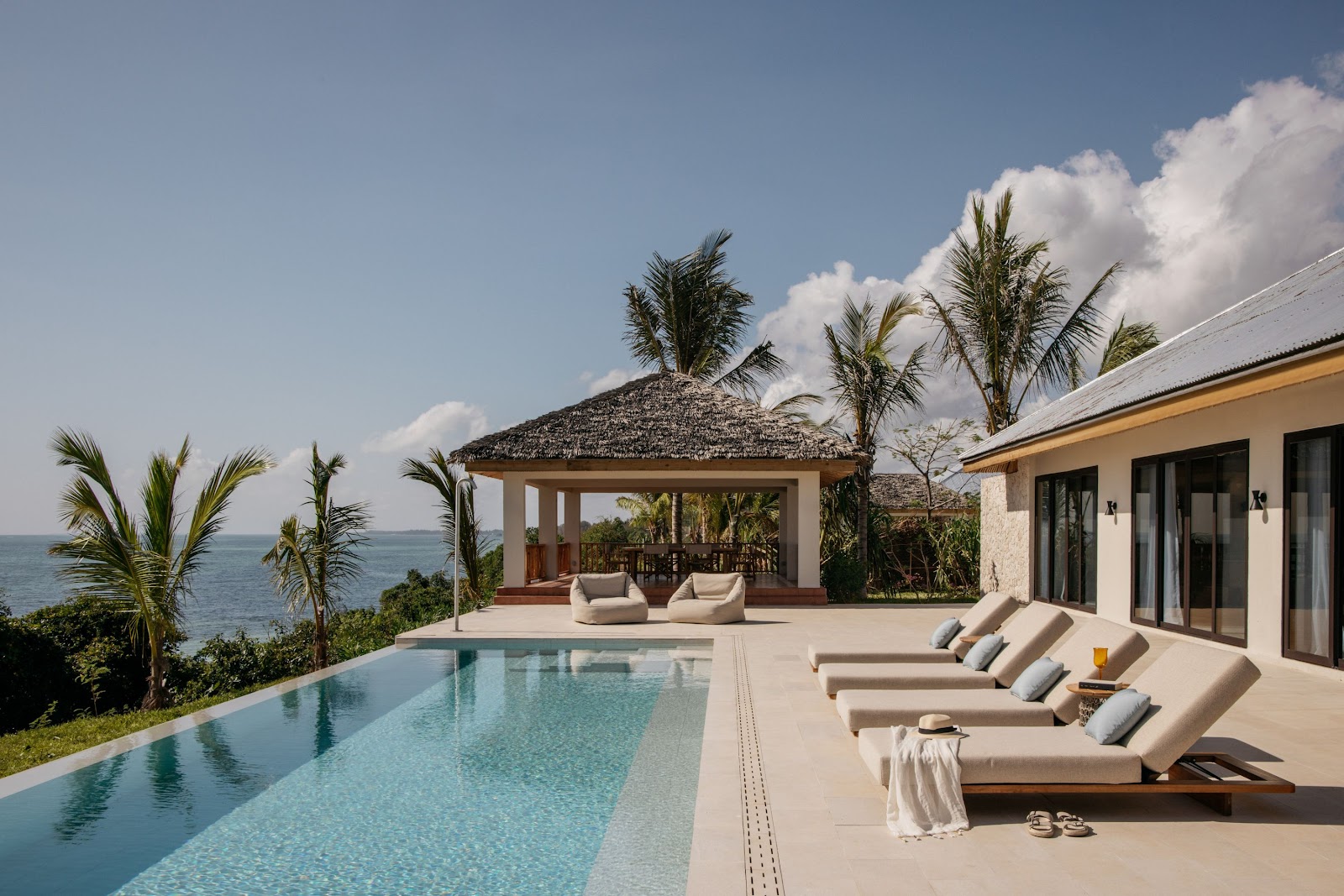 Infinity pool with lounge chairs overlooking the ocean at Meliá Zanzibar, with a thatched-roof pavilion and palm trees.