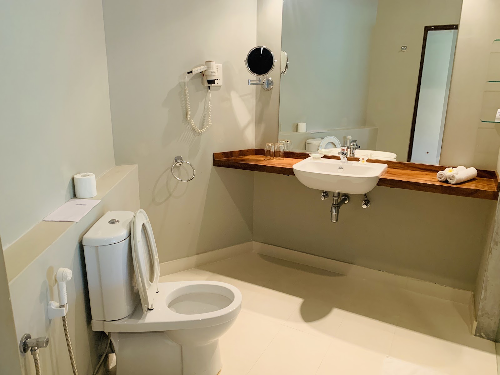 Bathroom with cream-colored walls, white toilet, wooden-trimmed sink vanity, illuminated mirror, and bathtub at the Mermaid Hotel & Club.