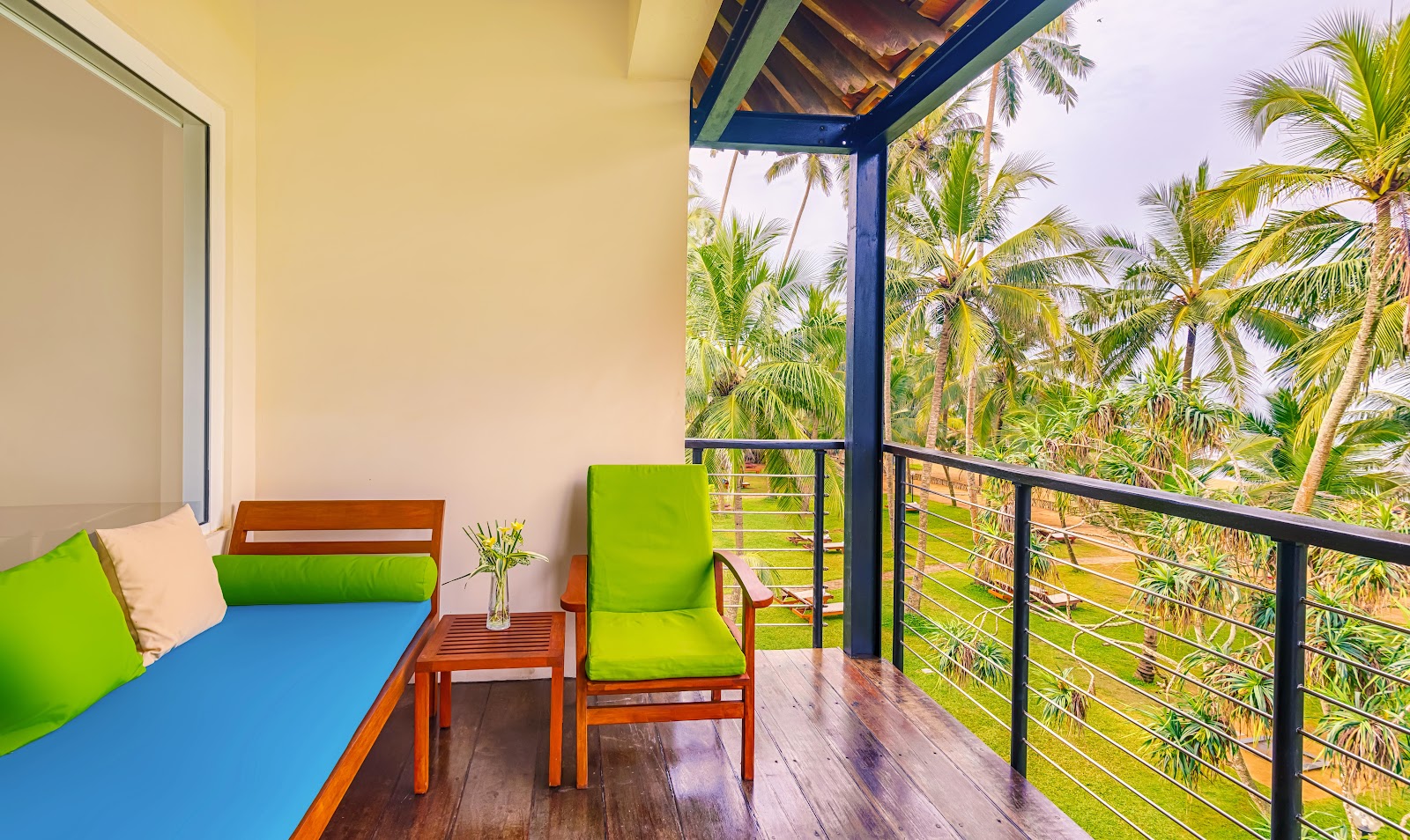 Balcony with lime-green cushioned chairs, blue lounger, and views of palm trees at Mermaid Hotel & Club.
