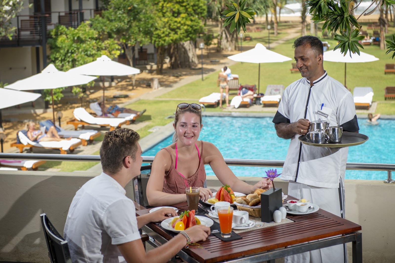 Guests play cricket on a grass field with palm trees and a brick building in the background at Mermaid Hotel & Club.