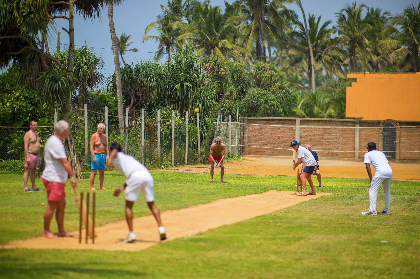 Wooden lounge chairs and benches scattered across a manicured lawn dotted with tall palm trees in front of the Mermaid Hotel & Club's multi-story colonial-style buildings.