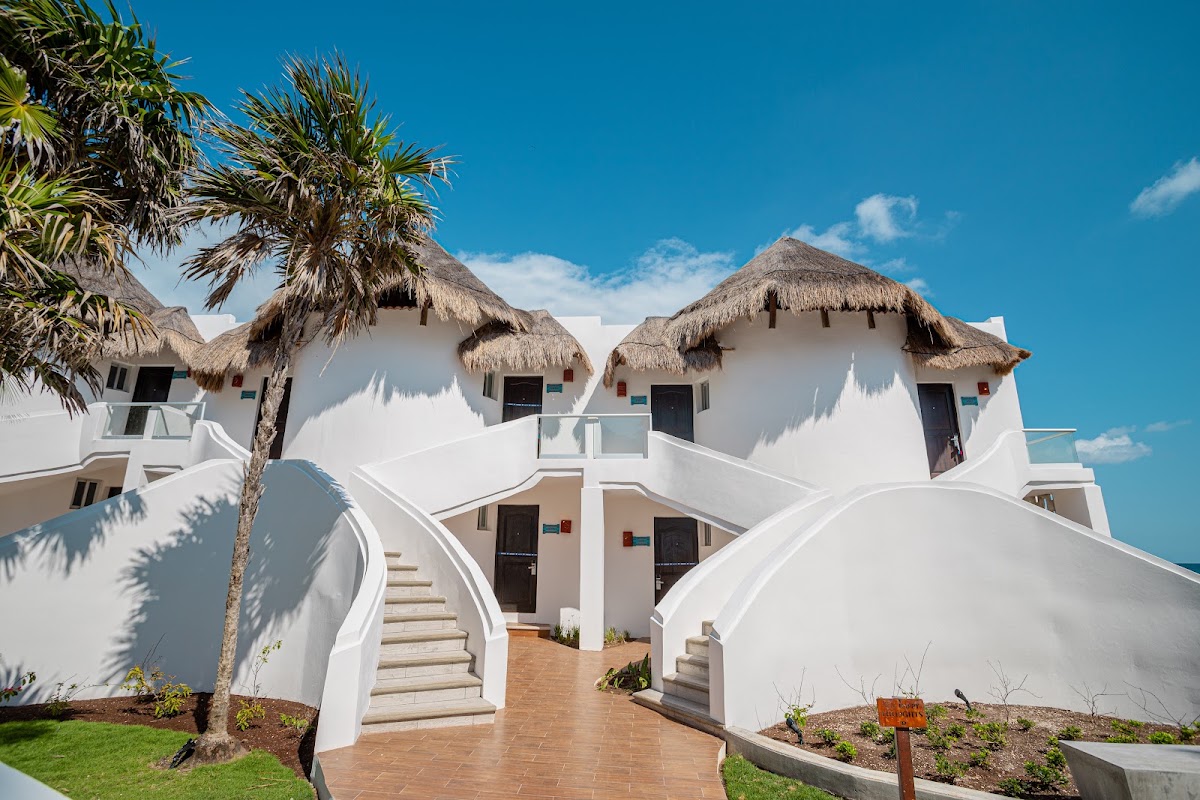 White bungalows with thatched roofs and curved staircases at MIA Reef Isla Mujeres, with palm trees and clear blue sky.