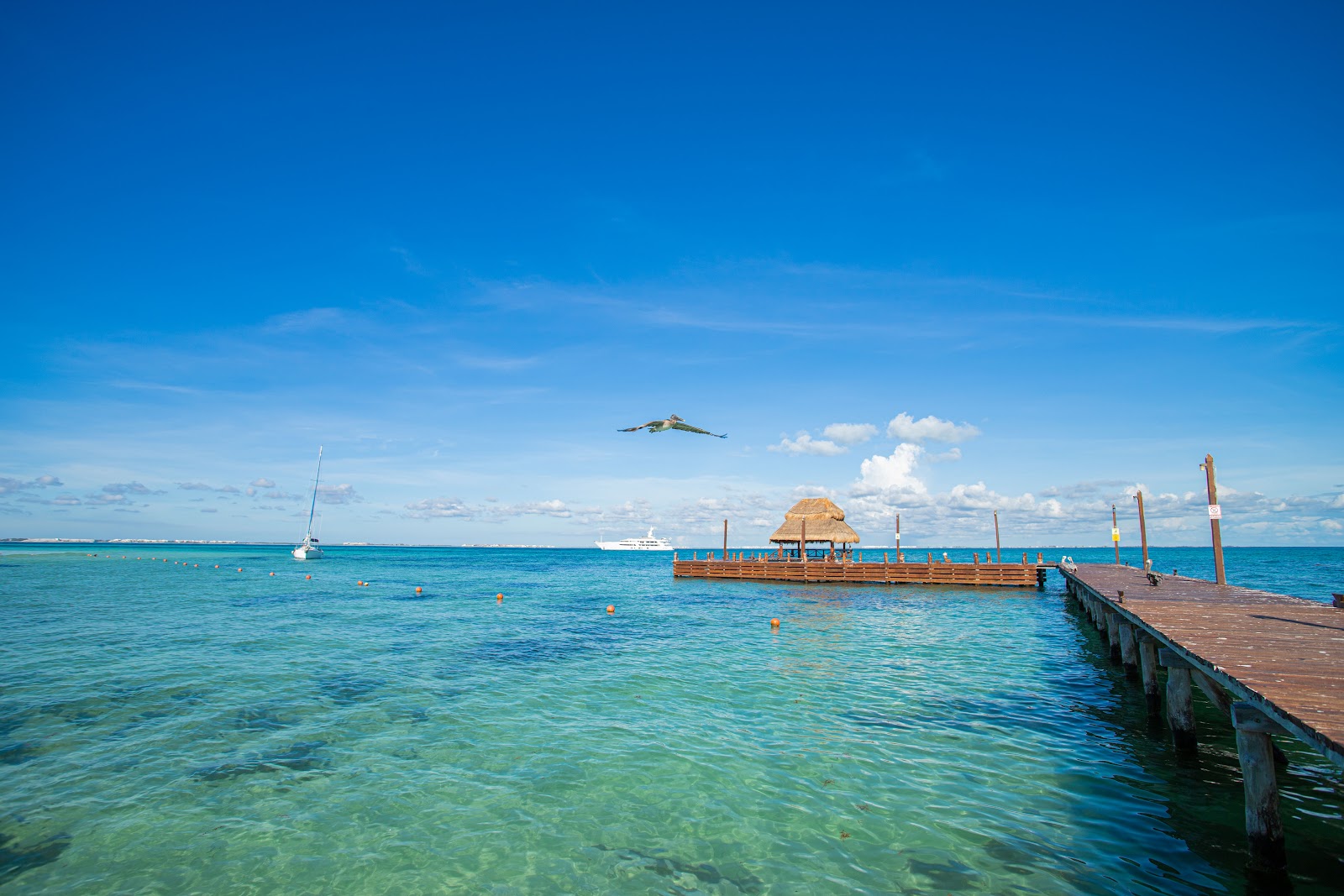 Wooden cabanas with string lights line a sandy beach at dusk, with calm turquoise water and palm fronds visible above.