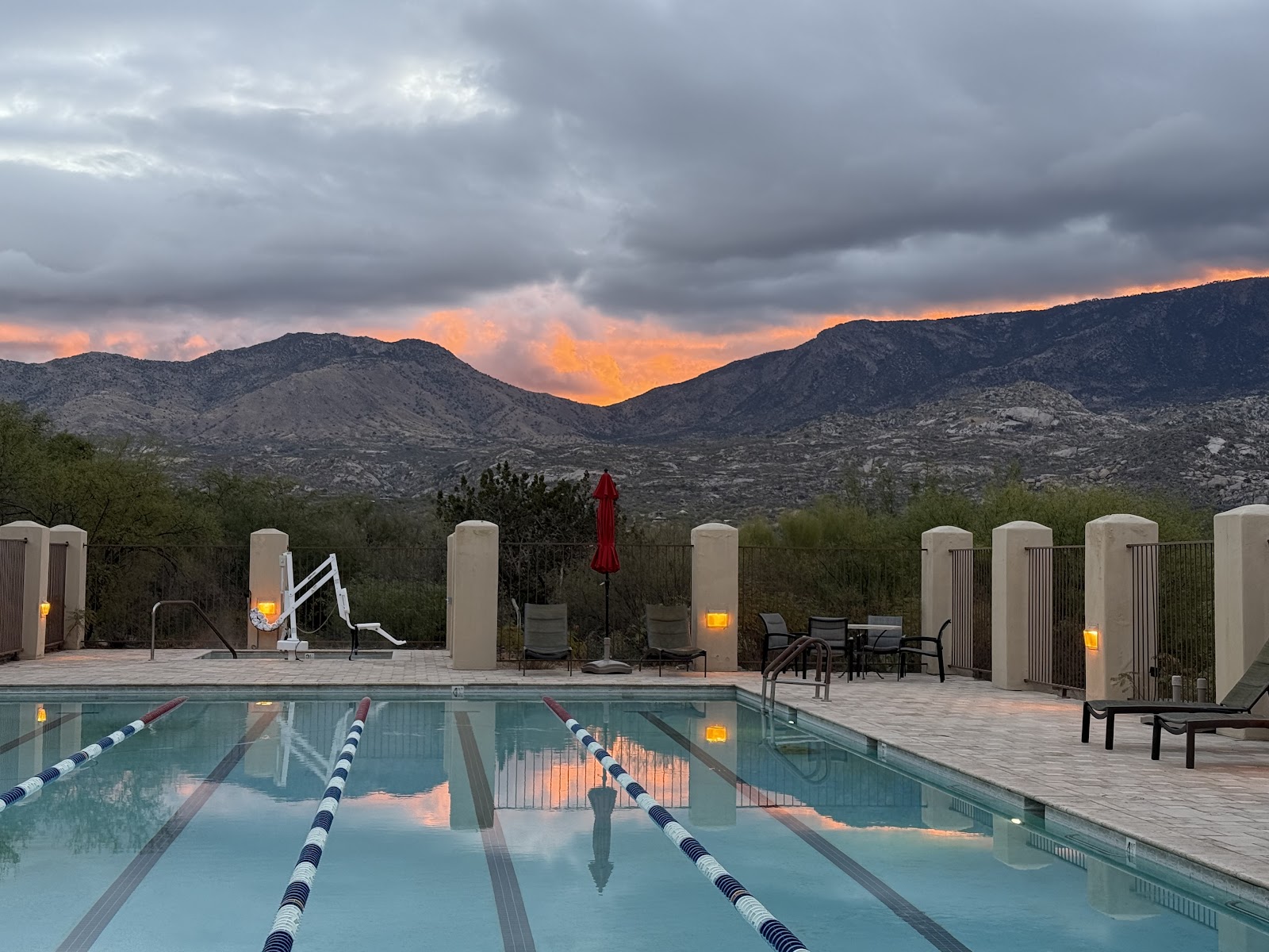 Lap pool with lane dividers at sunset, desert mountains glowing orange beyond the deck with lounge chairs and cabanas.
