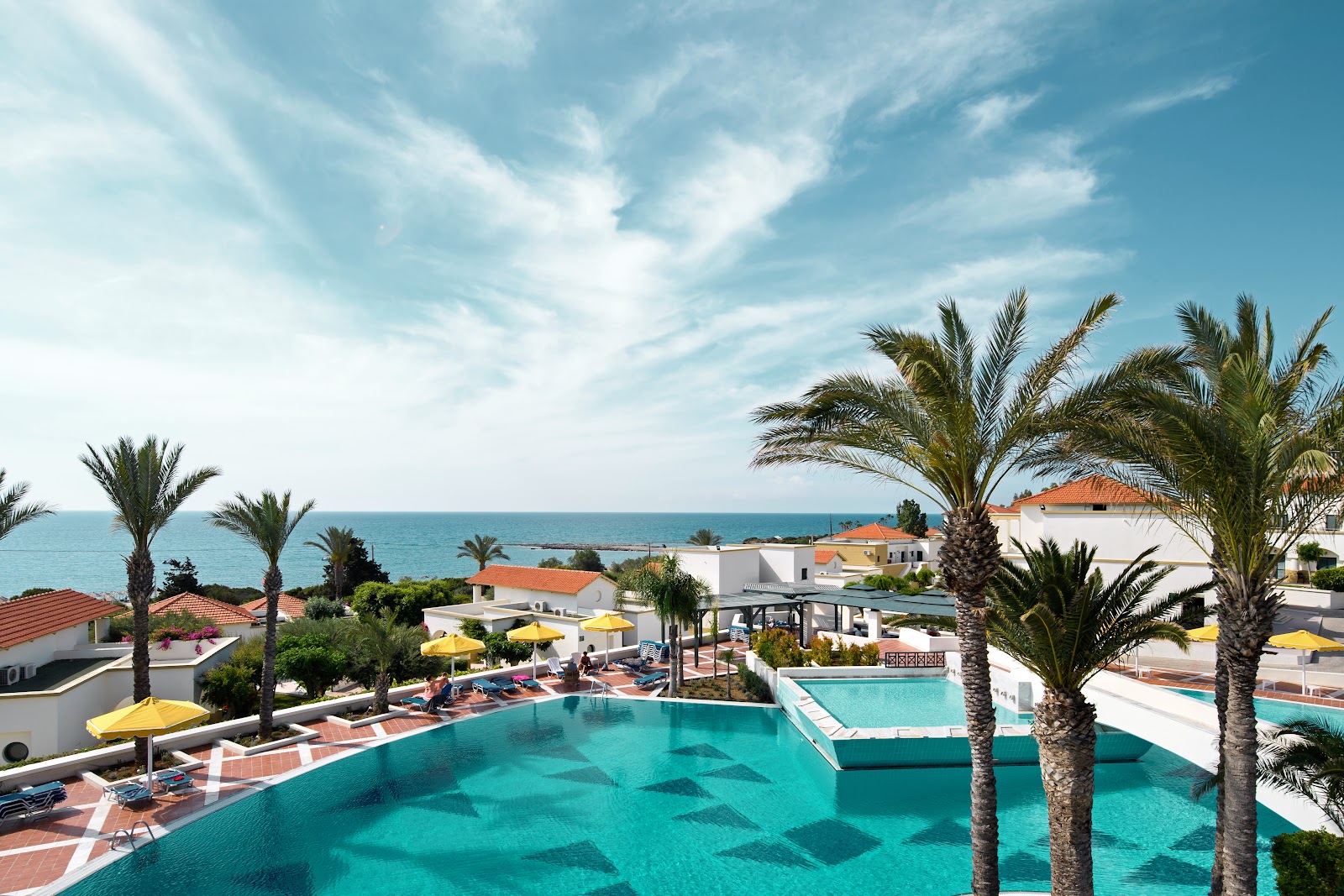 Turquoise pool with palm trees overlooks Mediterranean Sea and white resort buildings with terracotta roofs at Mitsis Rodos Maris.