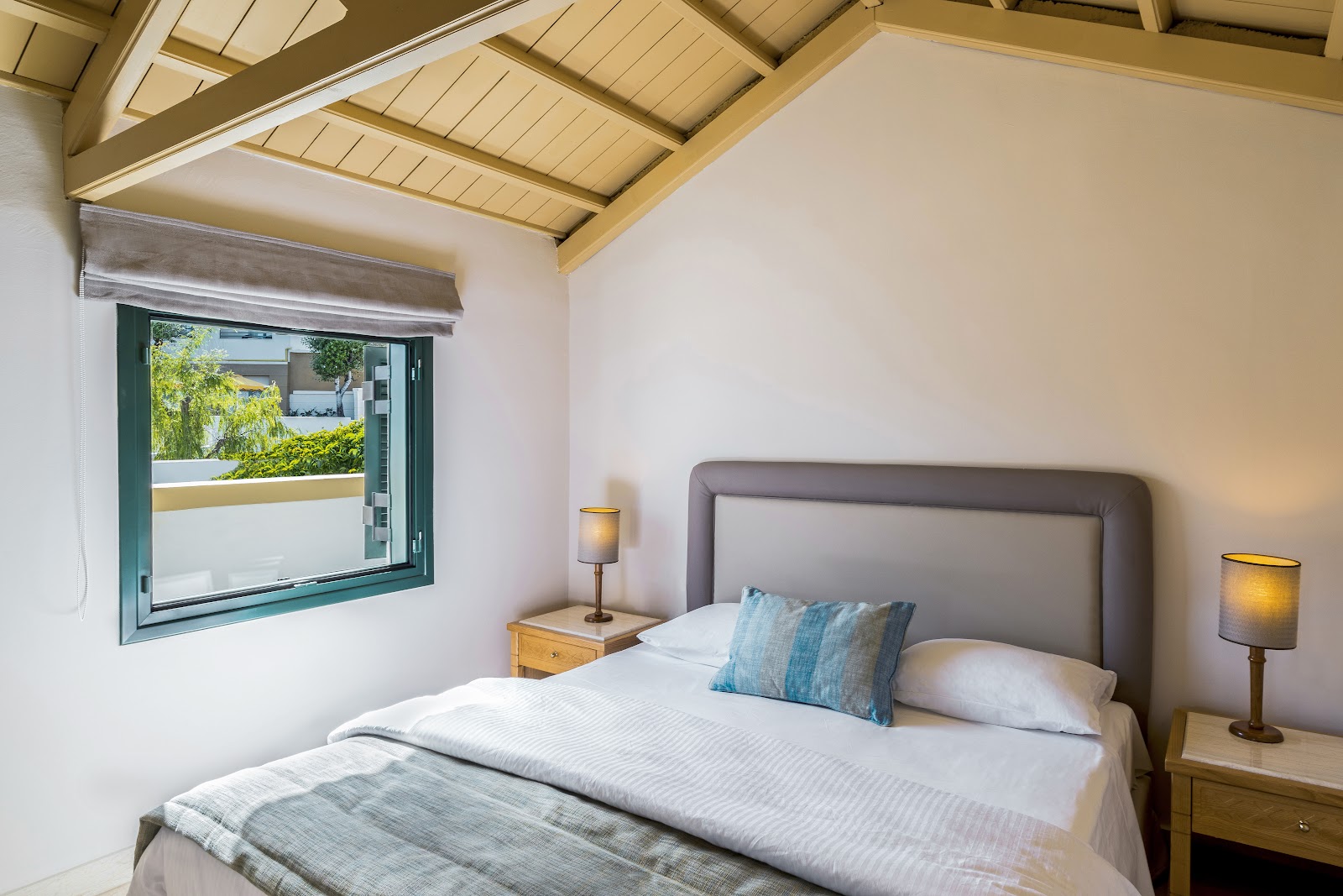 Resort bedroom with wooden desk, white orchids, bed with turquoise pillow, and cream sofa with green leaf-patterned cushions.