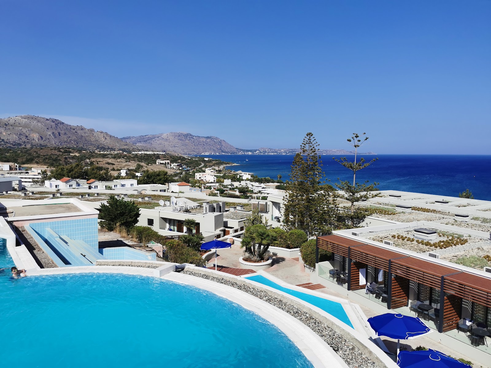 Water park with blue and orange twisting slides, a sailboat-shaped water feature, and spray fountains at Mitsis Rodos Village under clear sky.