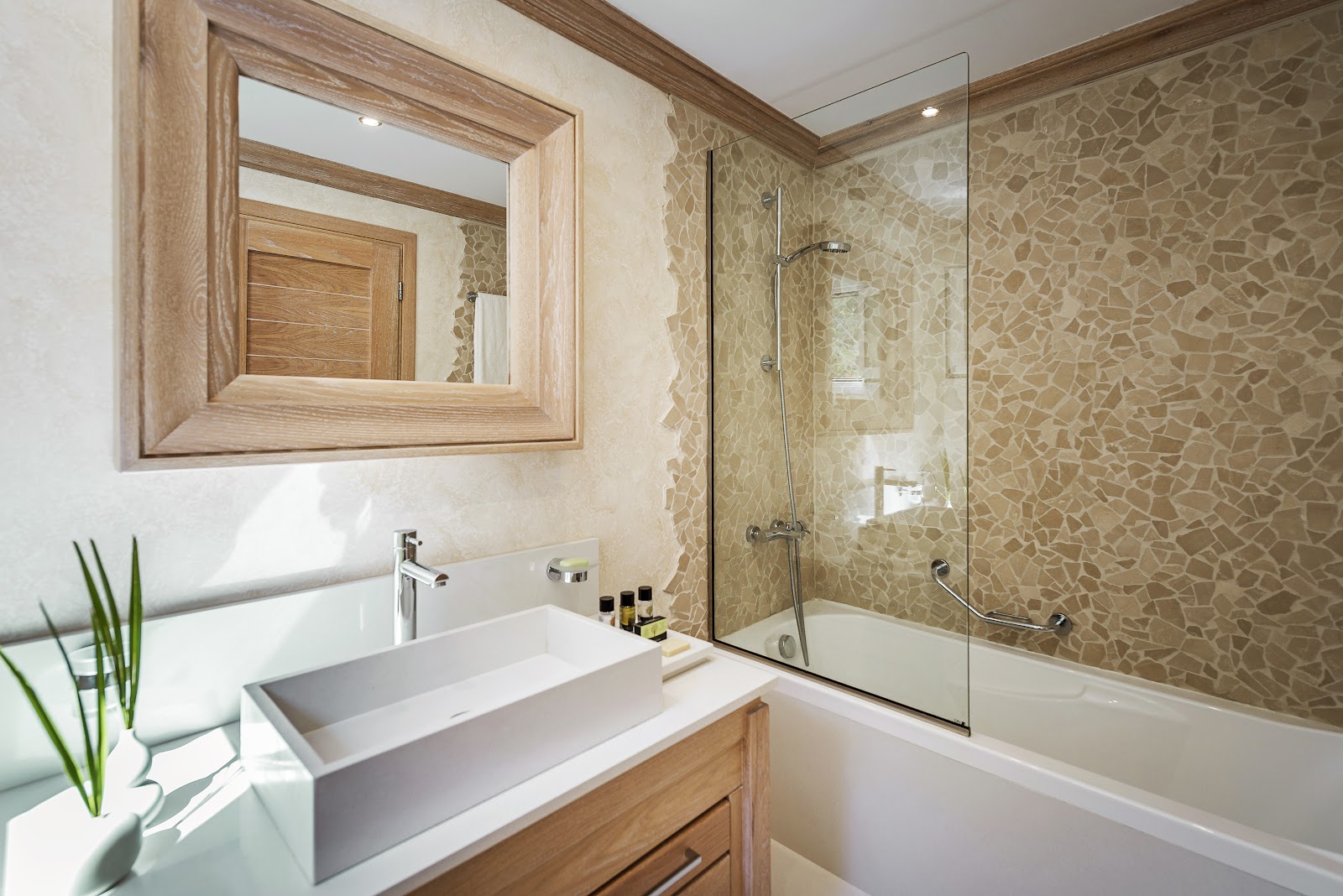 Modern bathroom with wooden vanity, rectangular sink, framed mirror, and glass-enclosed shower with mosaic tile walls.