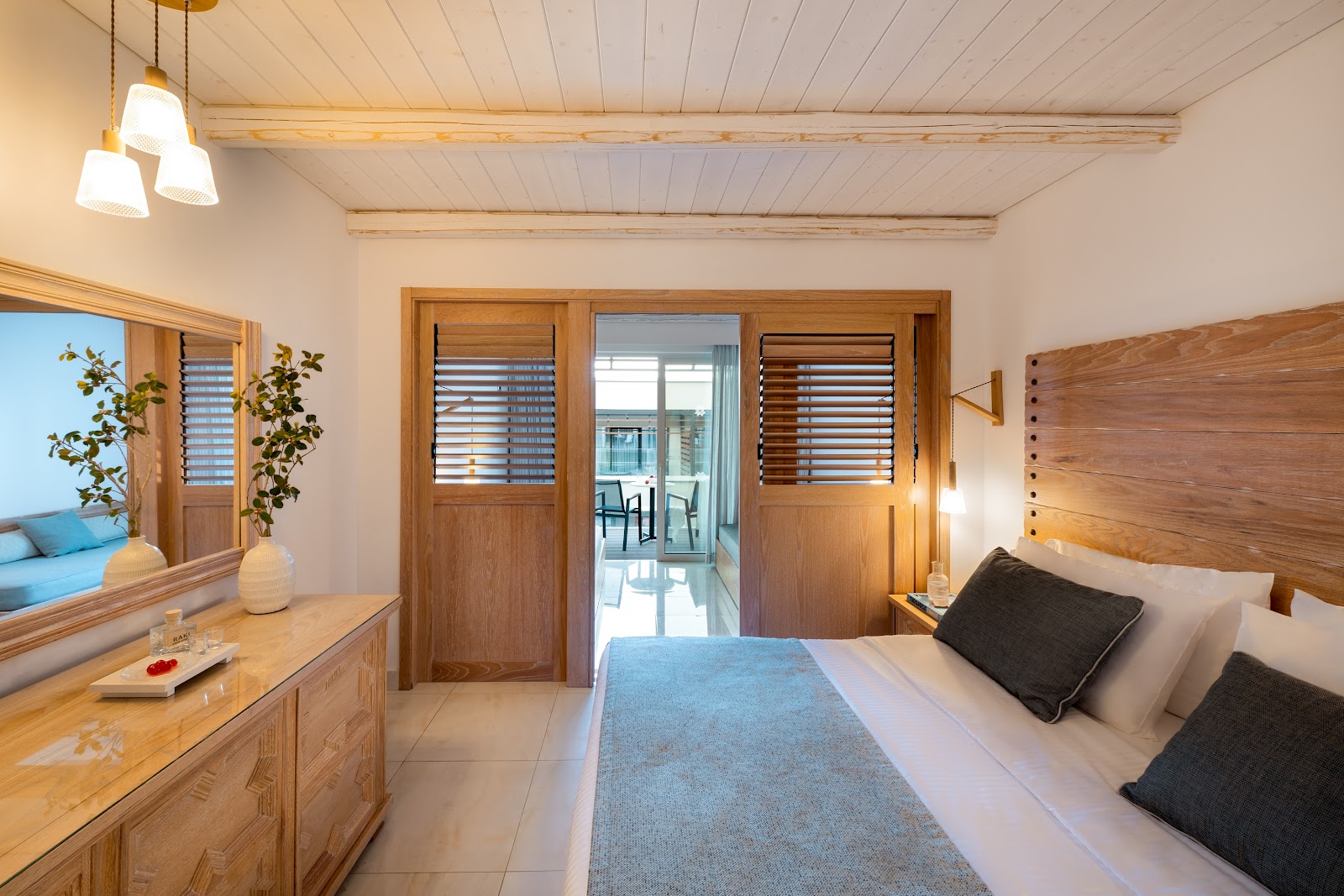 Resort bedroom with wooden furnishings, queen bed, vanity with mirror, and glass doors opening to a sea-view balcony.