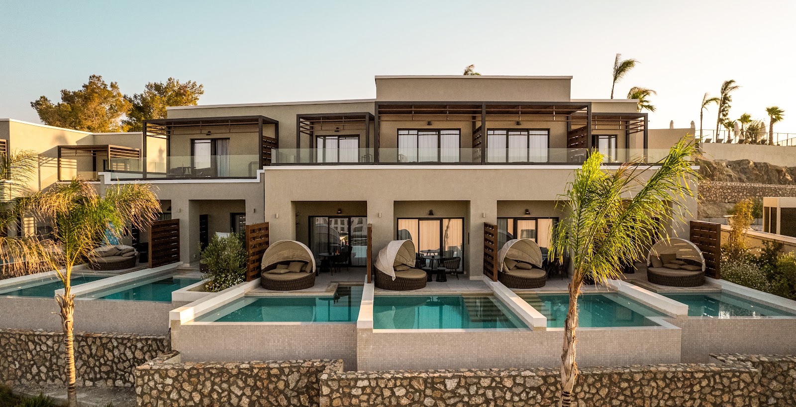 Fitness center at Mitsis Rodos Village with guests using cardio equipment, dumbbells, and machines beside floor-to-ceiling windows overlooking the sea.