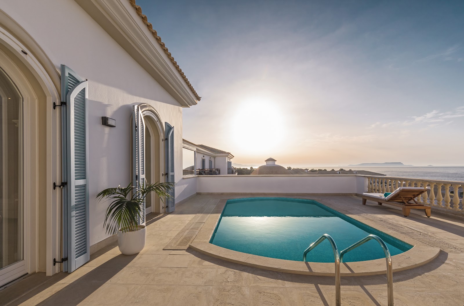 Private pool and terrace at Mitsis Selection Laguna overlook the beach and sea at sunset.