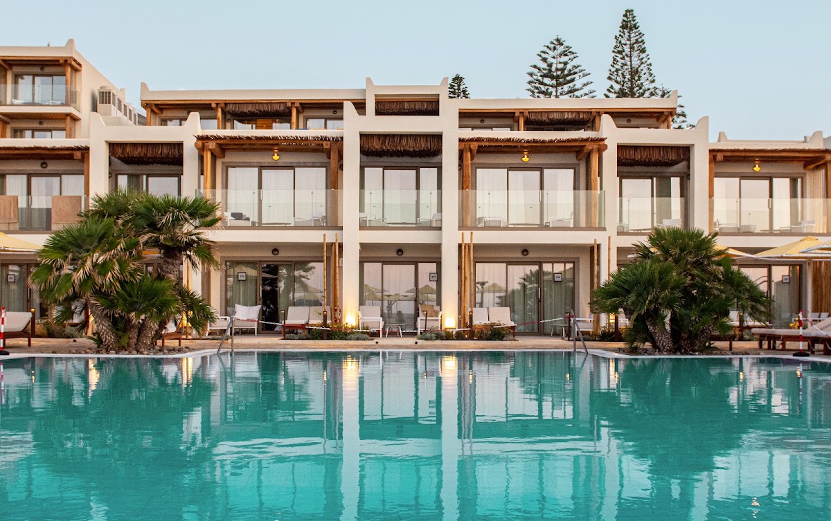 Turquoise pool fronts whitewashed buildings with wooden pergolas and palm trees at Mitsis Selection Rinela.