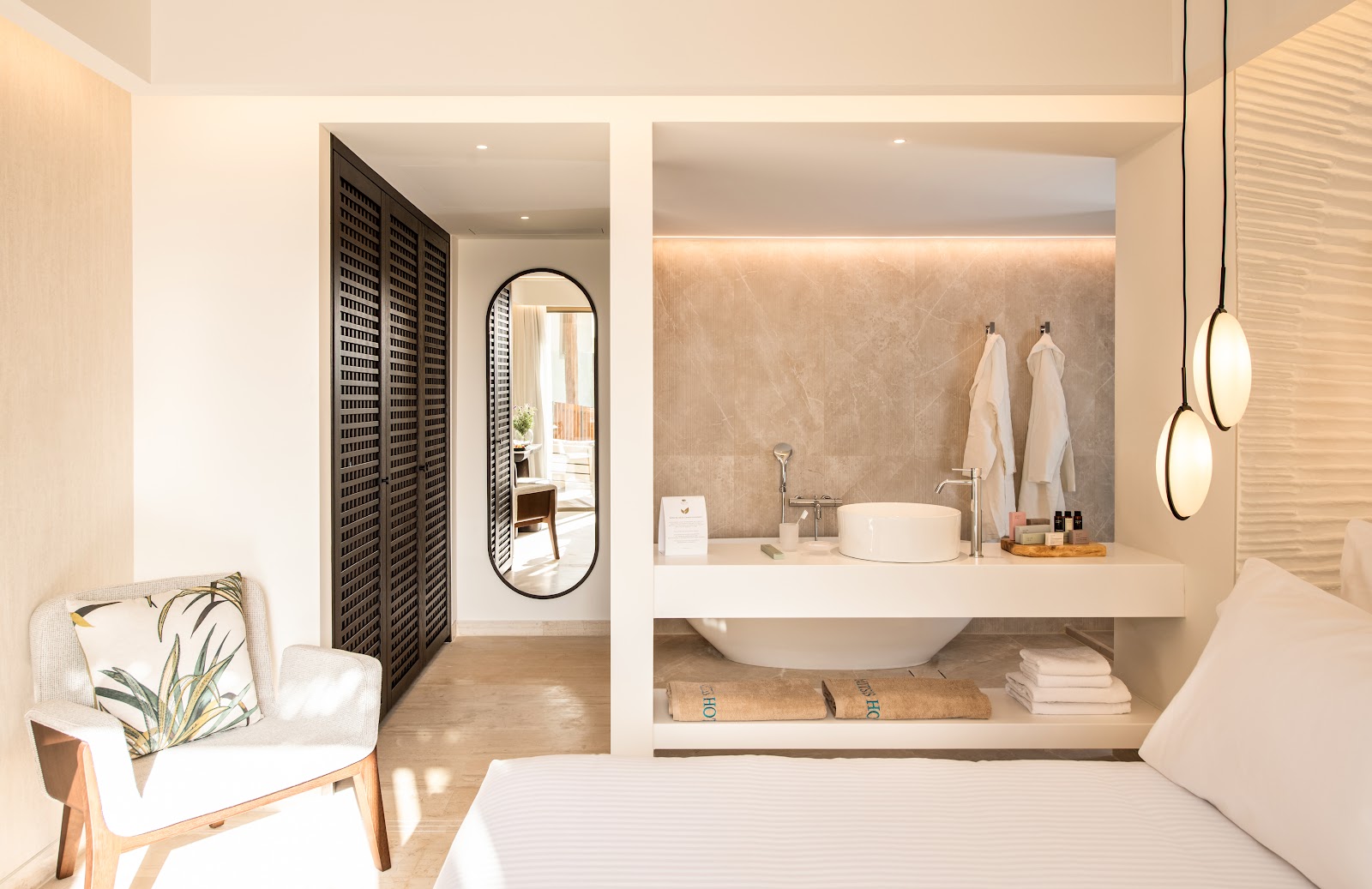 Spa-style bathroom with round vessel sink, floating vanity, pendant lights, white towels, and a view to the bedroom beyond through an arched mirror.