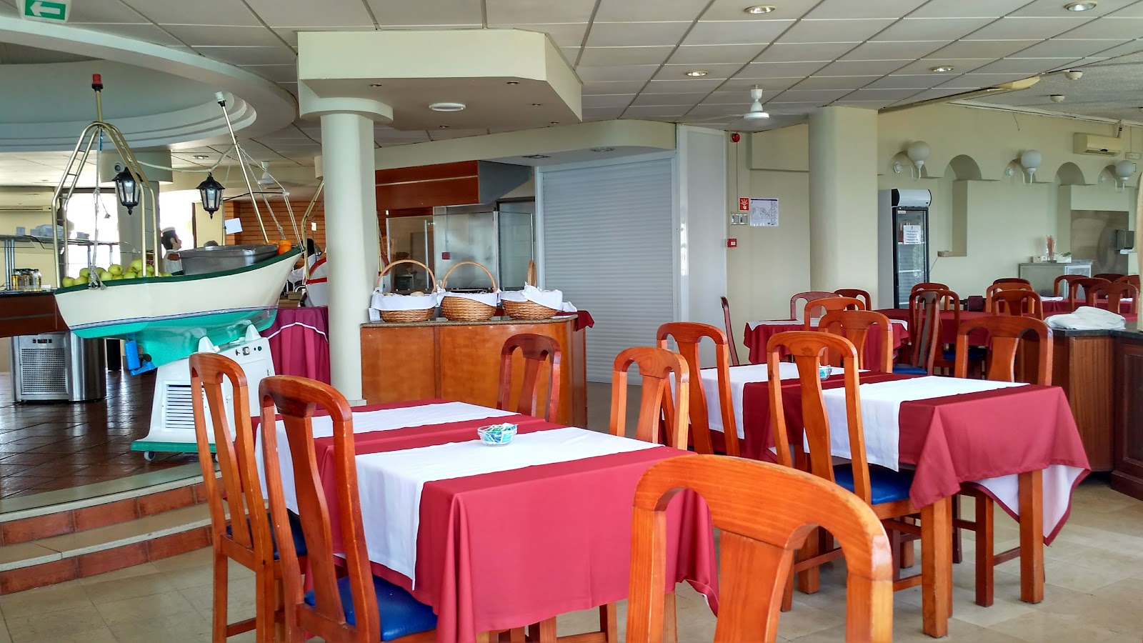 Dining room with wooden tables set with red and white linens, orange chairs, and a decorative fishing boat display in the corner.