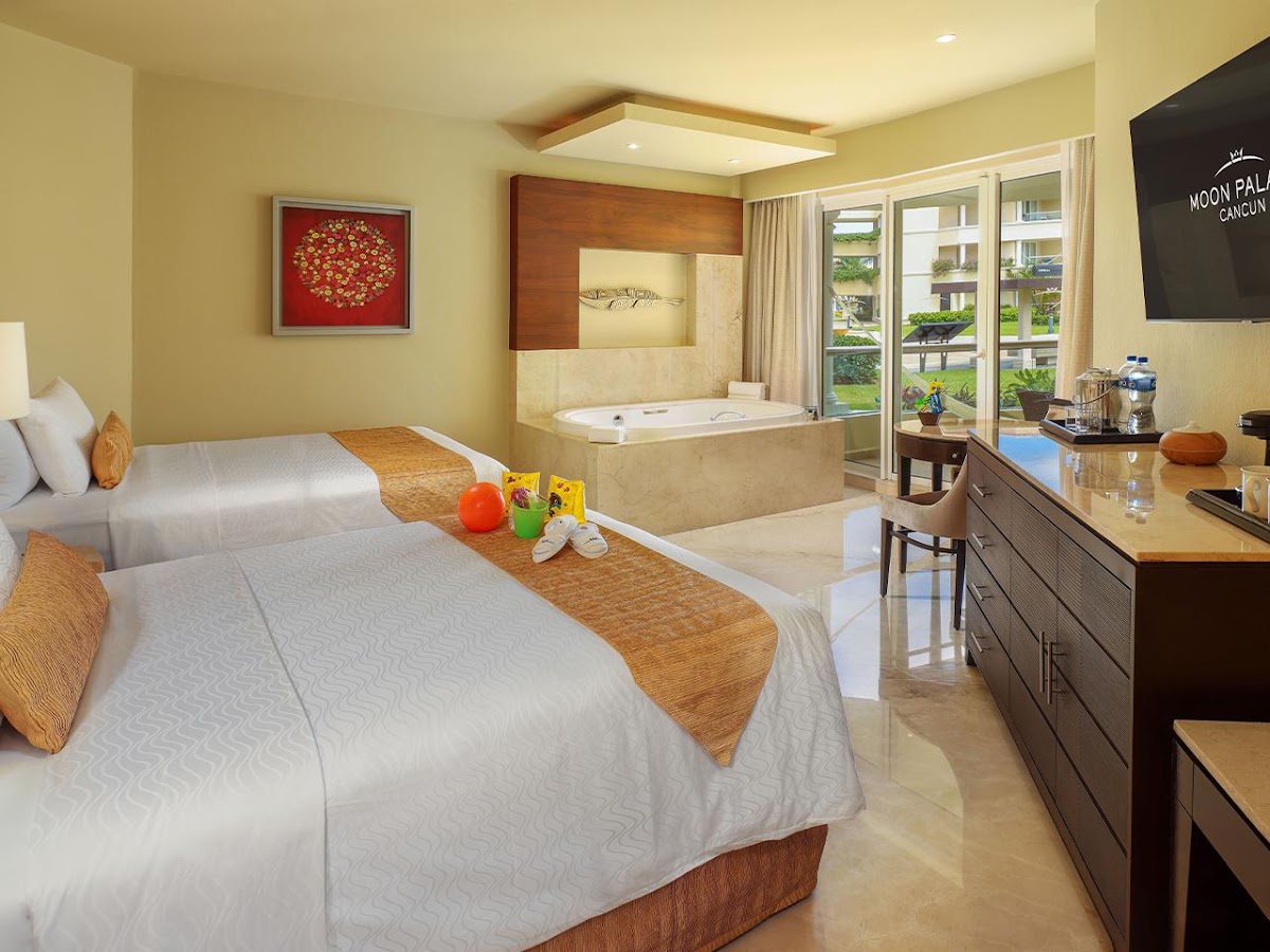 Moon Palace Cancun guest room with two beds, sunken whirlpool tub, and balcony overlooking tropical grounds.